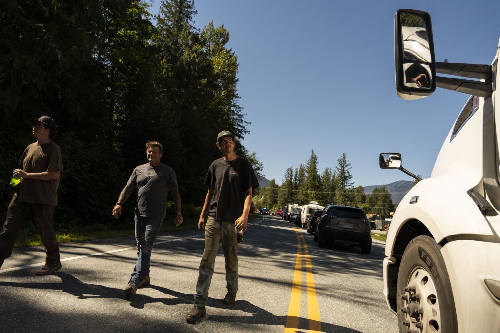 In Mount Currie, three men walk down Highway 99 alongside cars at a standstill due to a road block set up by First Nations in response to B.C.'s decision to open Joffre Lakes Park without their consent.