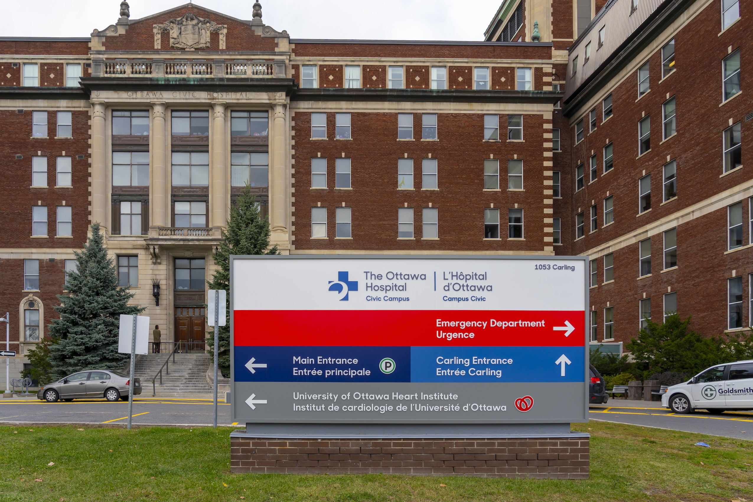 An exterior photograph of the Ottawa Hospital Civic Campus, including a sign directing people to the hospital's various entrances.