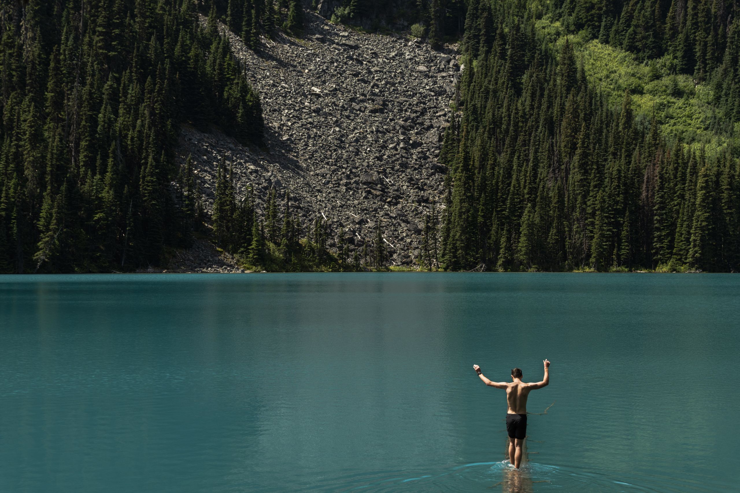 A hiker walks on the instagram famous log at for a photo at Middle Joffre Lake in Pipi7íyekw Joffre Lakes Provincial Park.