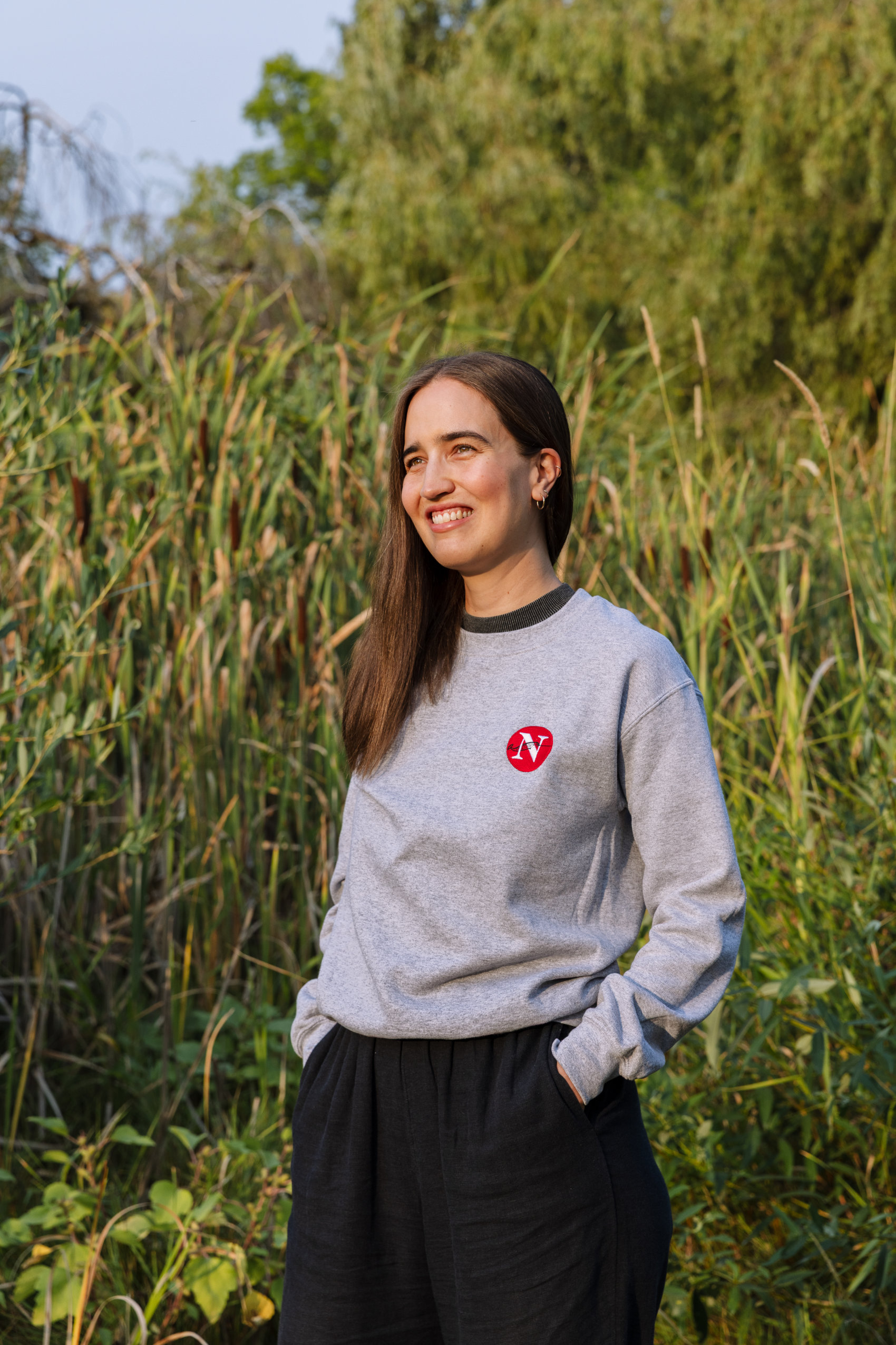 One of The Narwhal's new assistant editors, Paloma Pacheco, is seen standing in front of cattails and wearing a Narwhal sweatshirt.