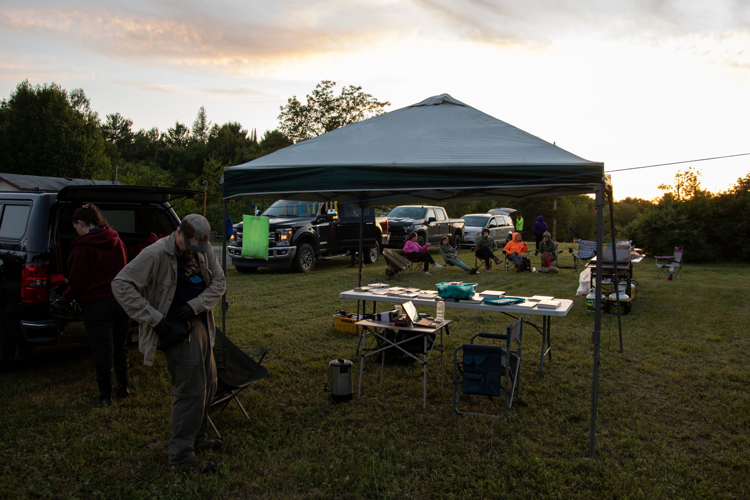 The processing tent at the Shawanaga community bat night, which includes a fold-out table covered in documents. A group of people are sitting in fold-out chairs in the background.