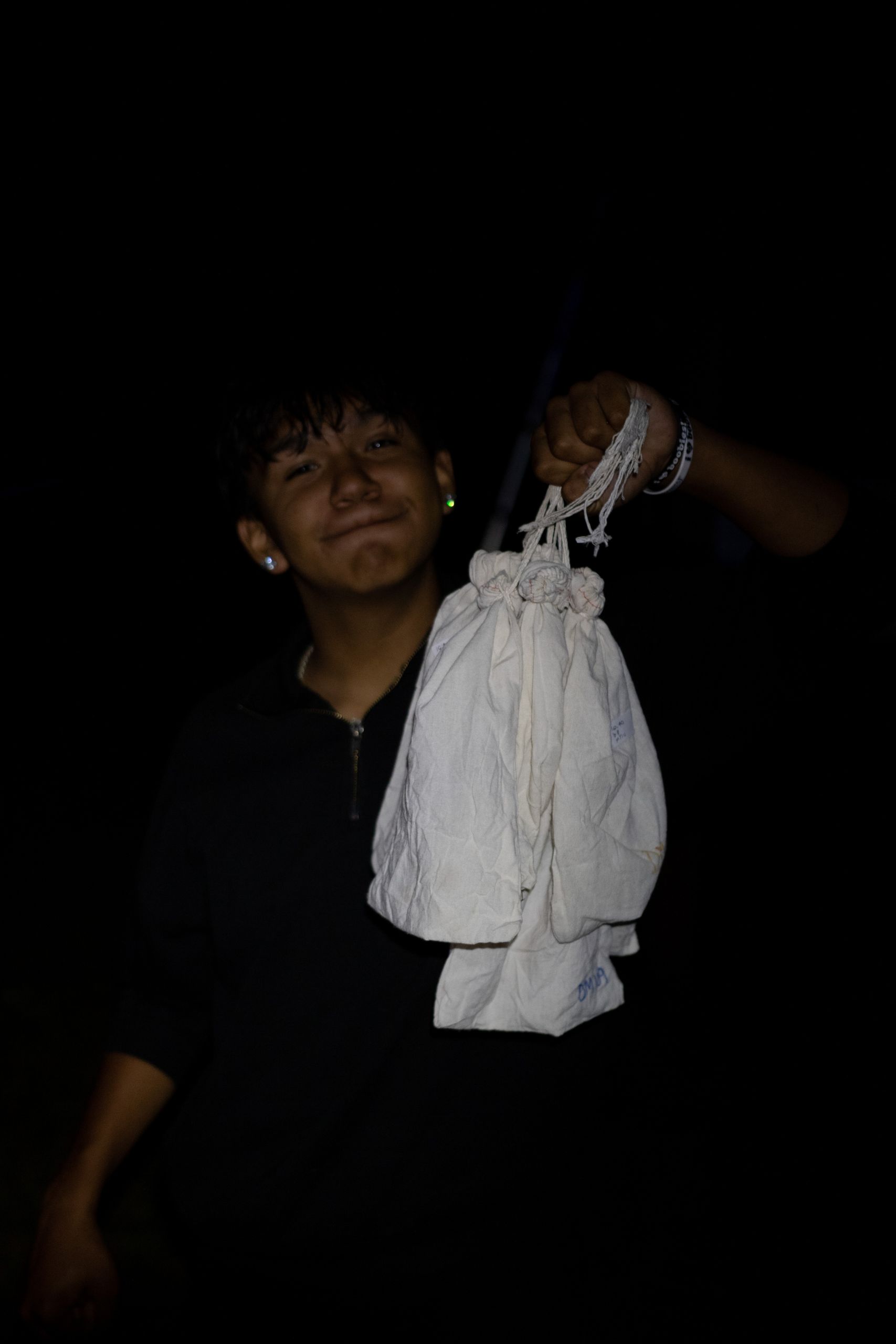 A young boy from the Shawanaga First Nation holding several white cloth bags of bats that will be measured, banded and released.