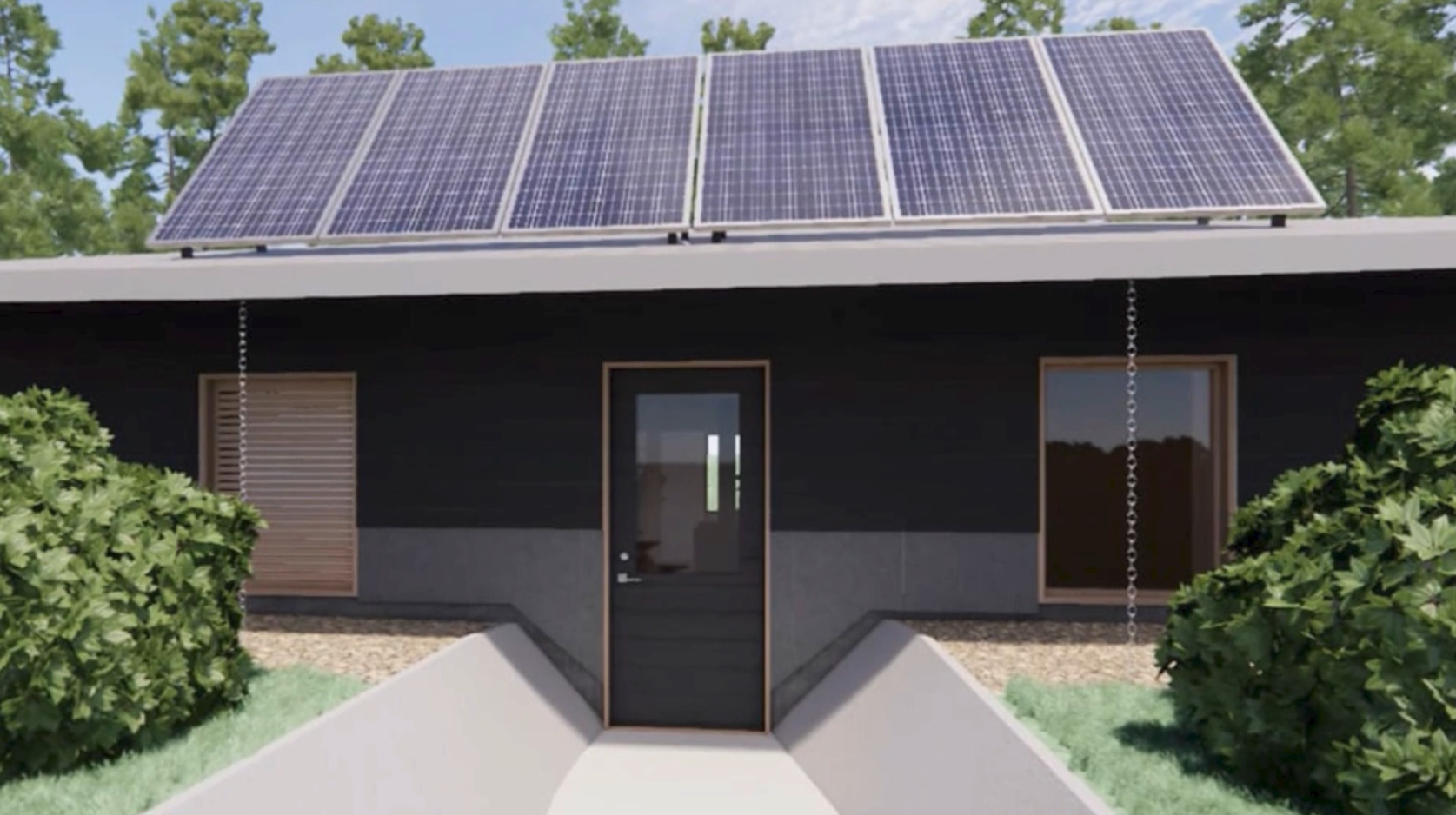 A Yunesit'in fire resisant house animated rendering shows the hoes entrance. It is set a bit into the ground, with dark walls, and solar panels over the black door, with green bushes on either side. The pathway leading to the door is paved and also set a little bit into the ground