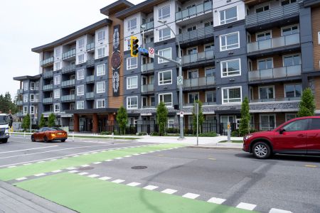 A large, five-storey housing complex on an urban street with Coast Salish artwork on the facade