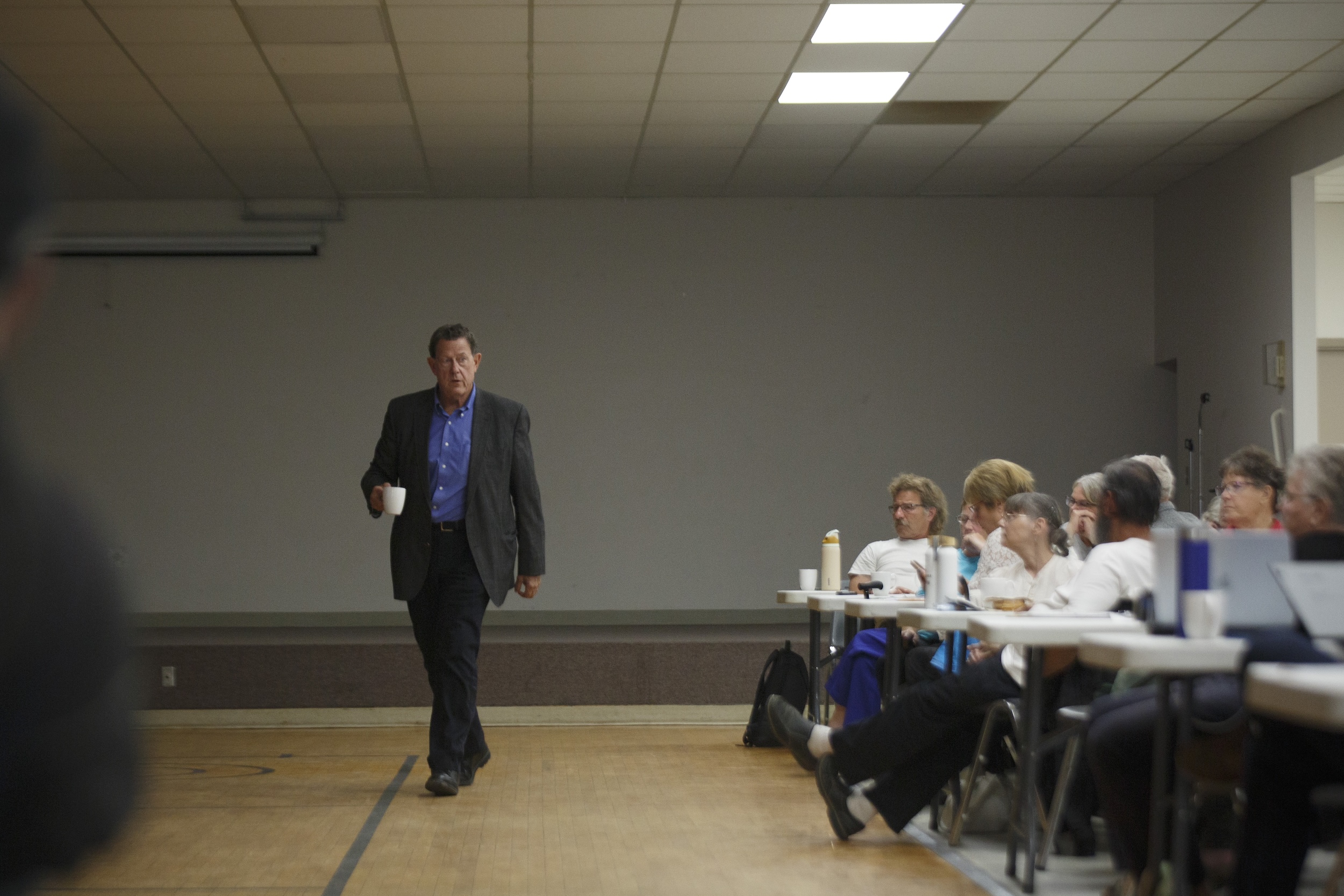 A government representative walks past a seated crowd of people at a surface rights meeting in Warburg, Alta.