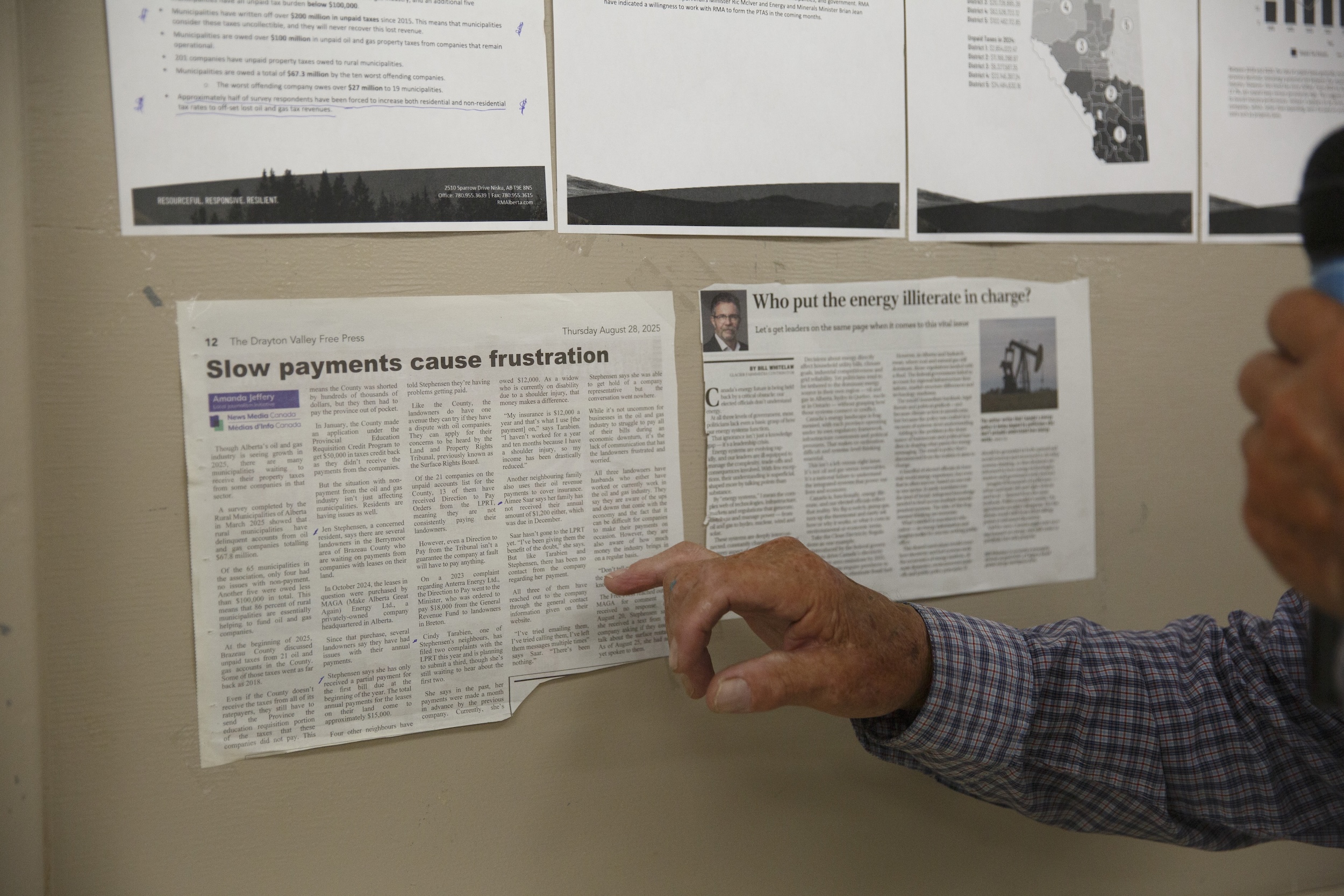 A man's hand points to a clipping of a news story pinned to a corkboard at a surface rights meeting in Walburg, Alta.