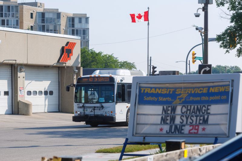 A Winnipeg Transit bus flashing a "Sorry not in service" banner leaves the city transit garage. A sign outside the garage announces the new system starting June 29