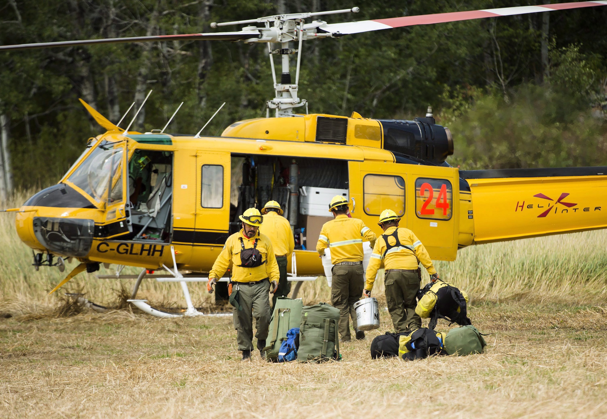 Four firefighters load gear onto a landed helicopter.