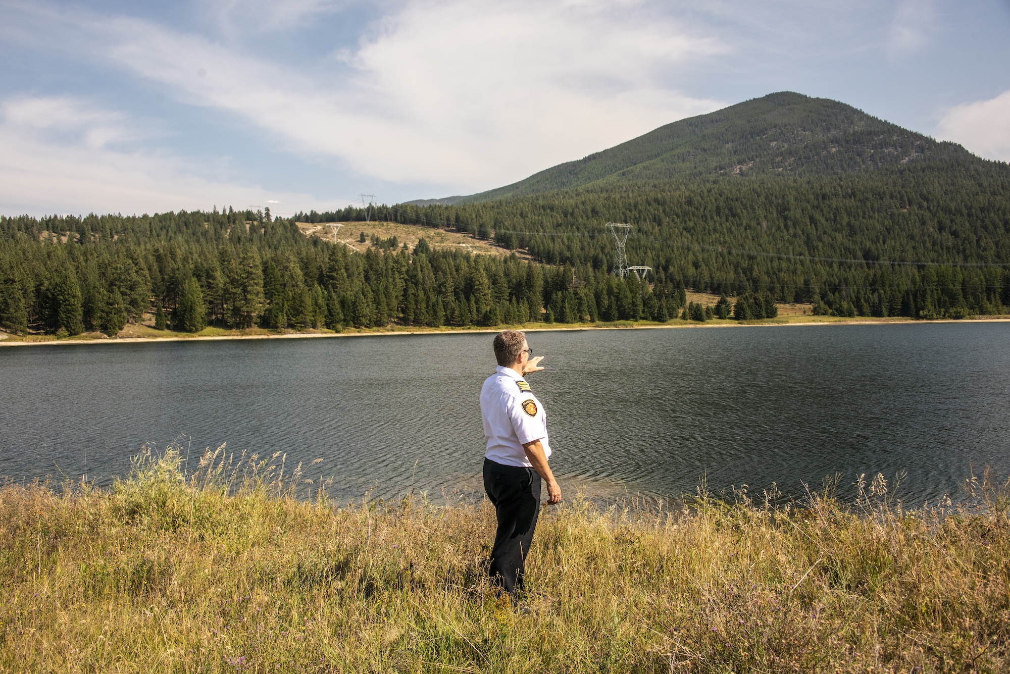 Cranbrook fire chief Scott Driver pointing to a hillside across a lake on the east shore of Cranbrook, B.C.