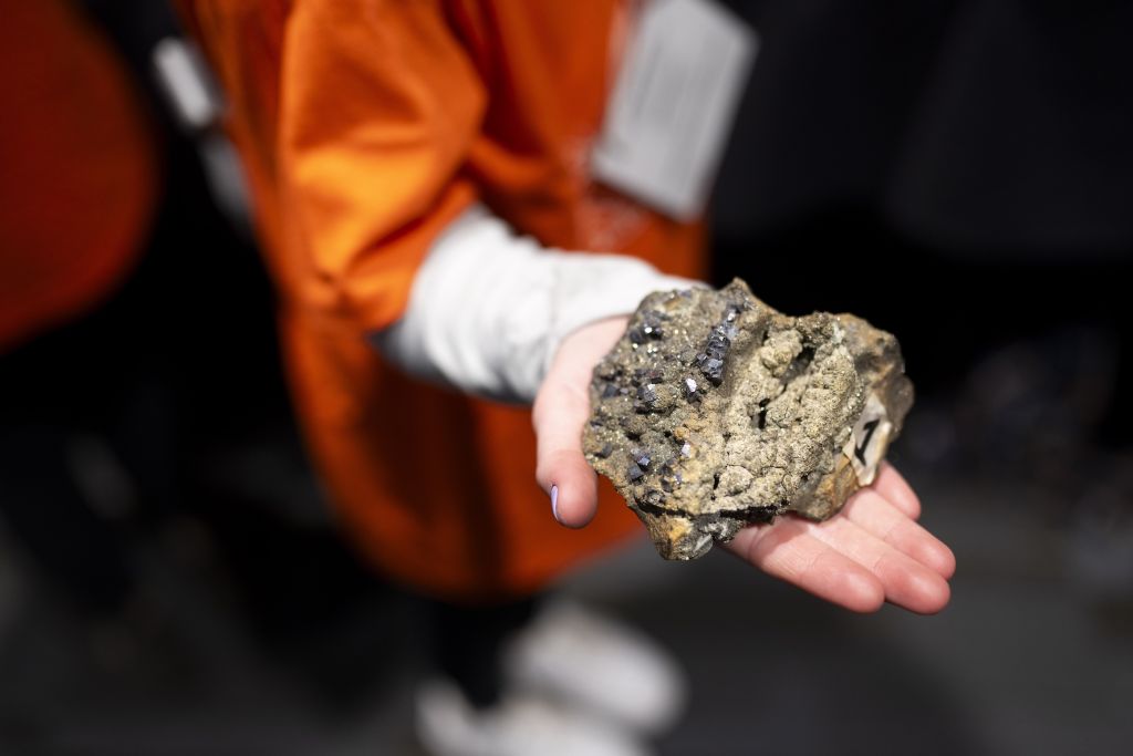 A closeup of a student's hand holding a rock sample during a conference on mineral exploration.