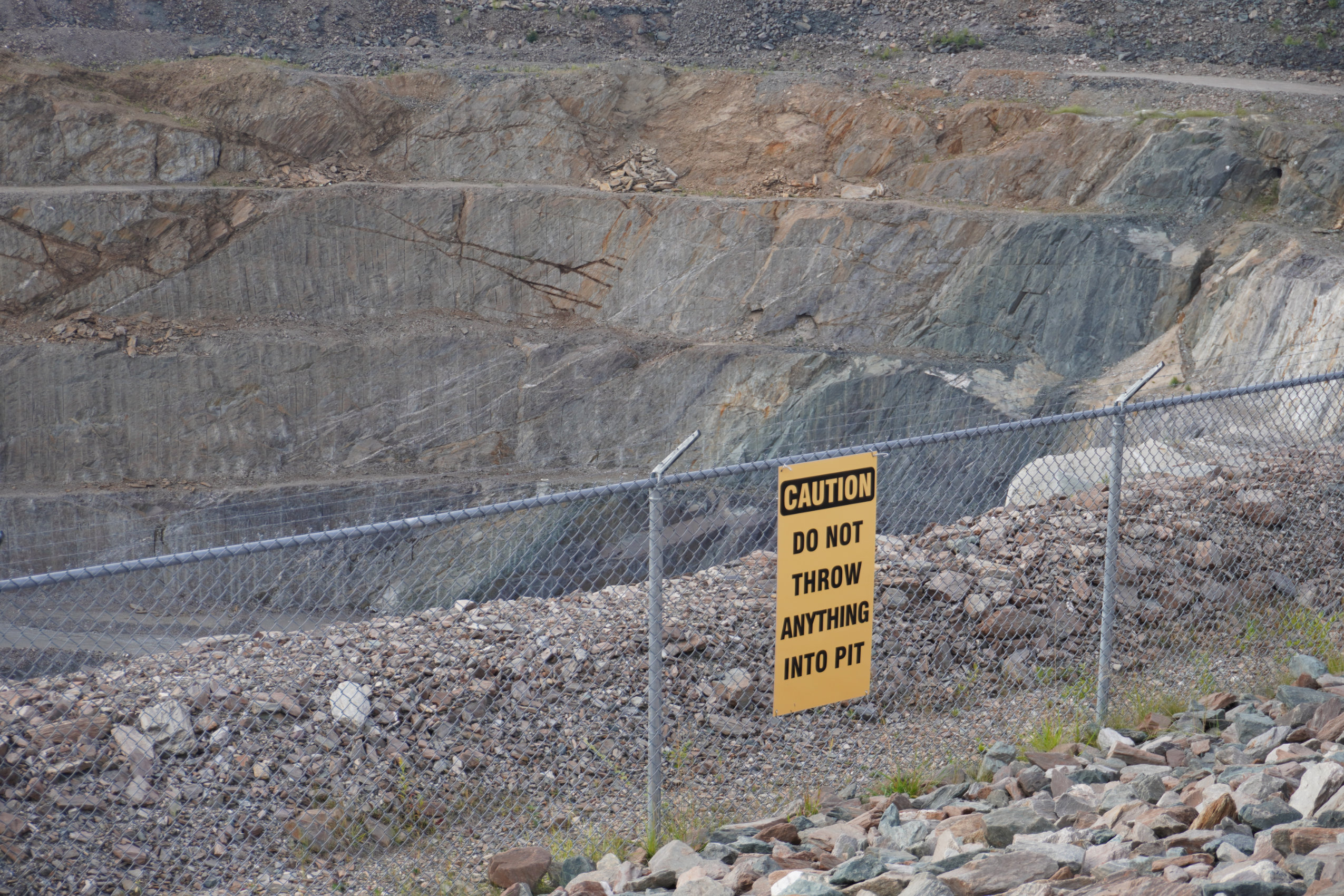 The decommissioned Hollinger open-pit gold mine in Timmins, Ont. A sign on a chain link fence reads "Caution. Do not throw anything into pit."