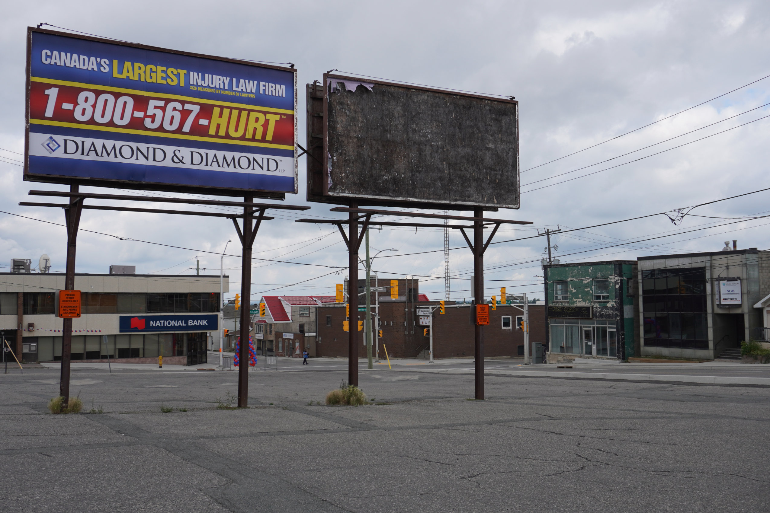 The downtown core of Timmins, Ont., which looks economically depressed. Weeds sprout through the cracks of an empty parking and paint peels off the front of a building in the background.