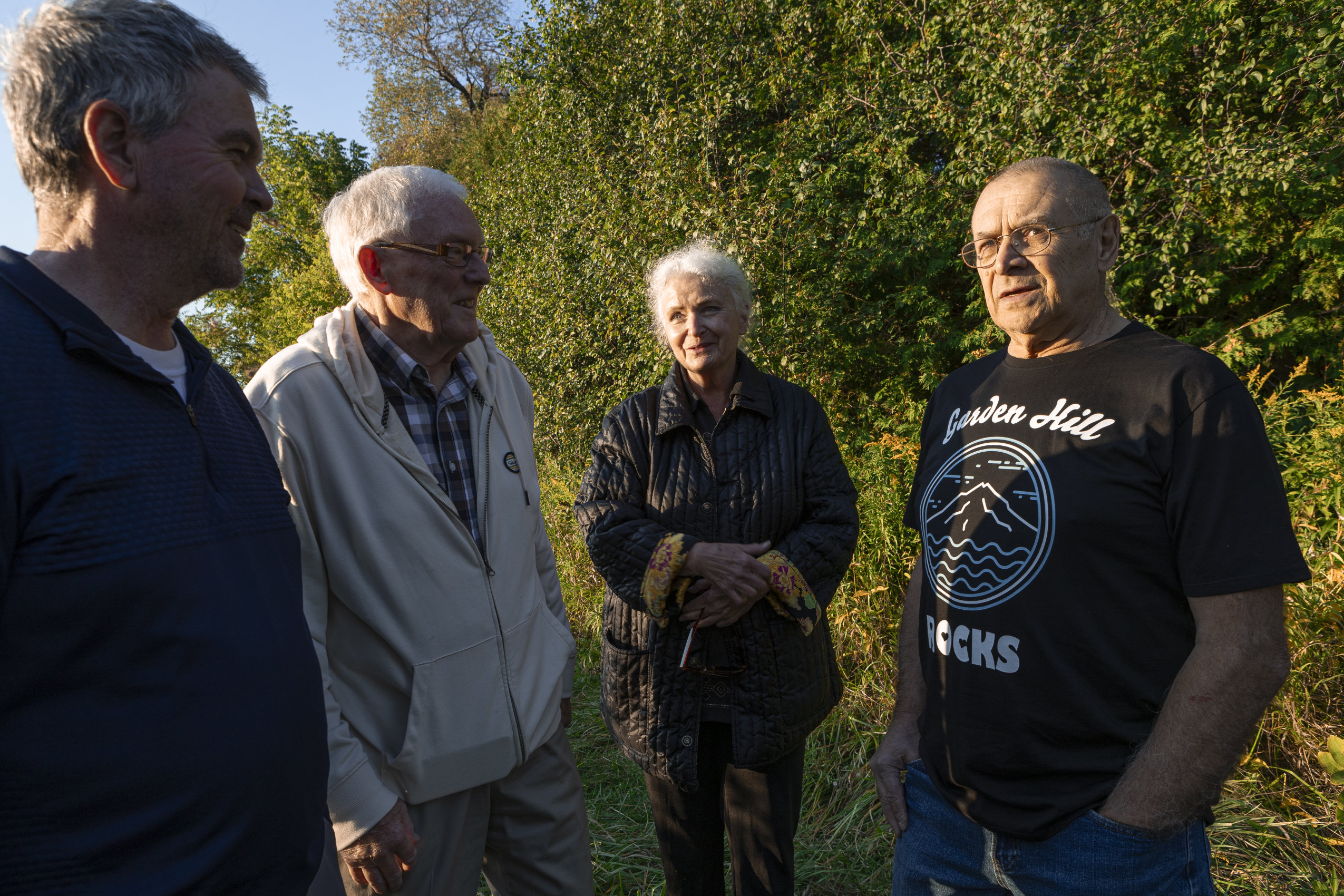 Richard Yoshida, Jane Zednik, Greg Burns and Glenn Deeth (right to left) stand talking in a circle, with a backdrop of trees and shrubs. All four are opponents of a recent decision to adjust the boundaries of a protected area in Port Hope, Ont.
