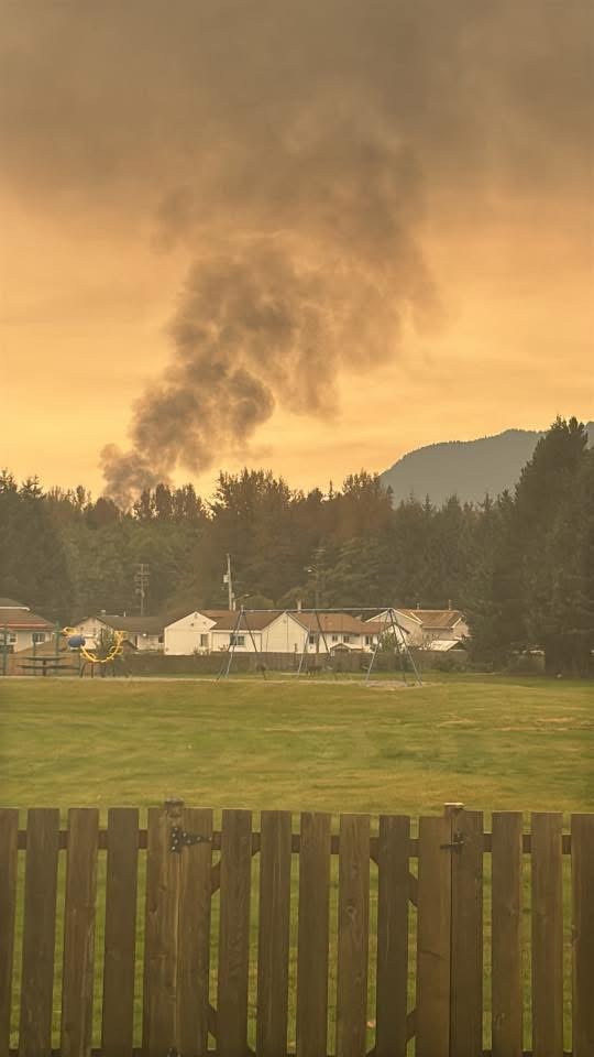 Smoke rising into the air above a forest and a group of houses in Kitimat, B.C.