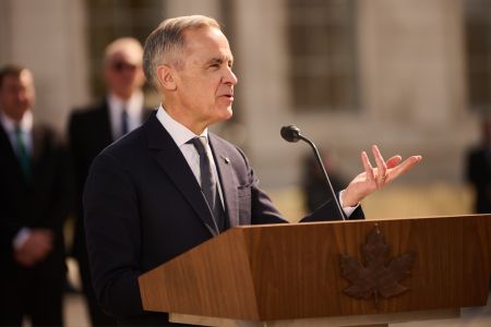 Mark Carney, in a dark suit, gestures with a hand as he speaks at a lectern
