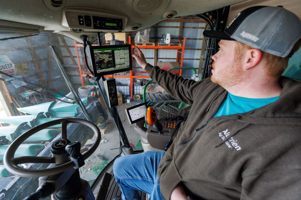 A man sits in a tractor fidding with a screen attached to the front of the vehicle.