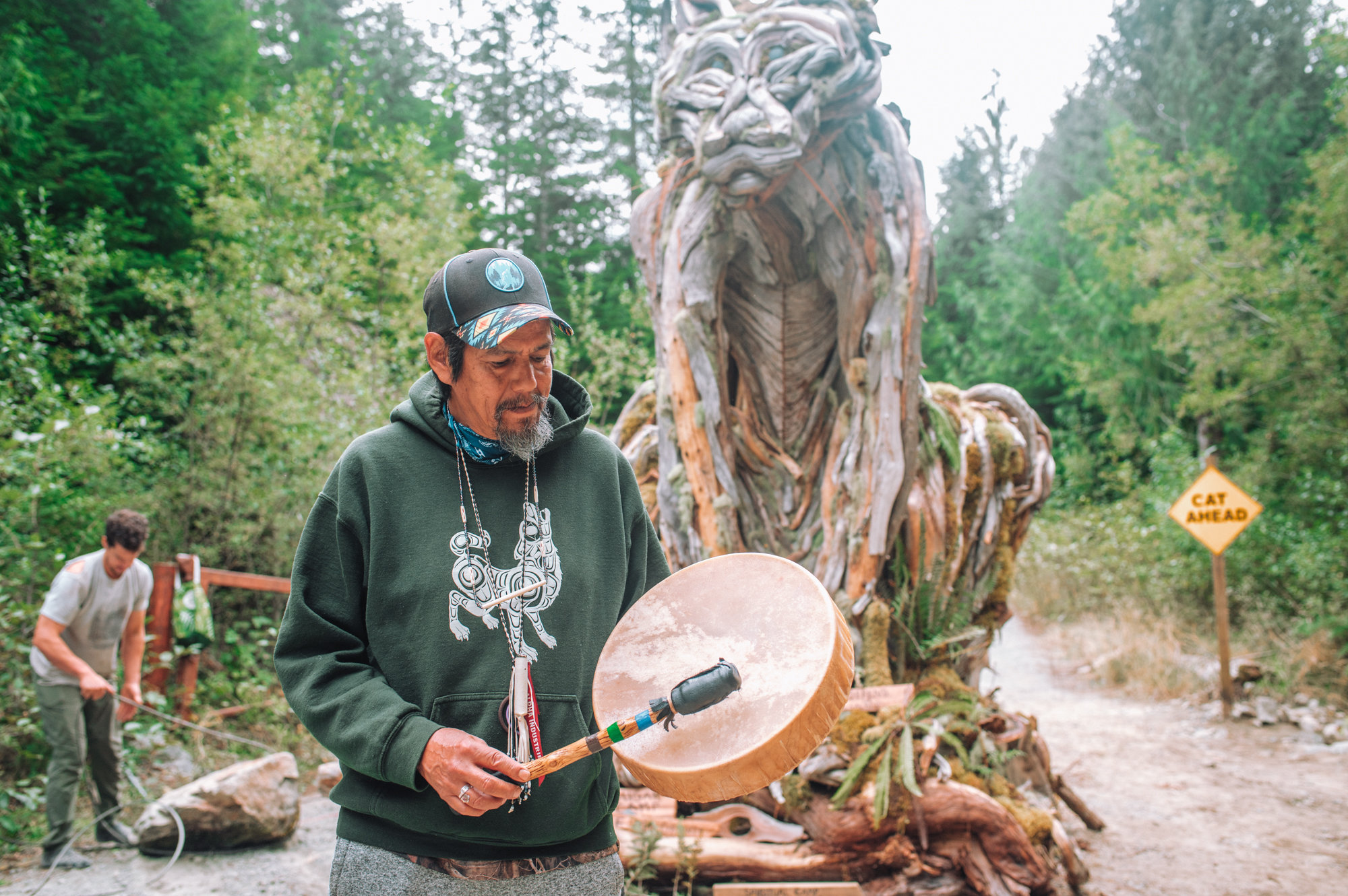 A man beats a drum in front of a log sculpture of a cat at the Walbran logging blockage