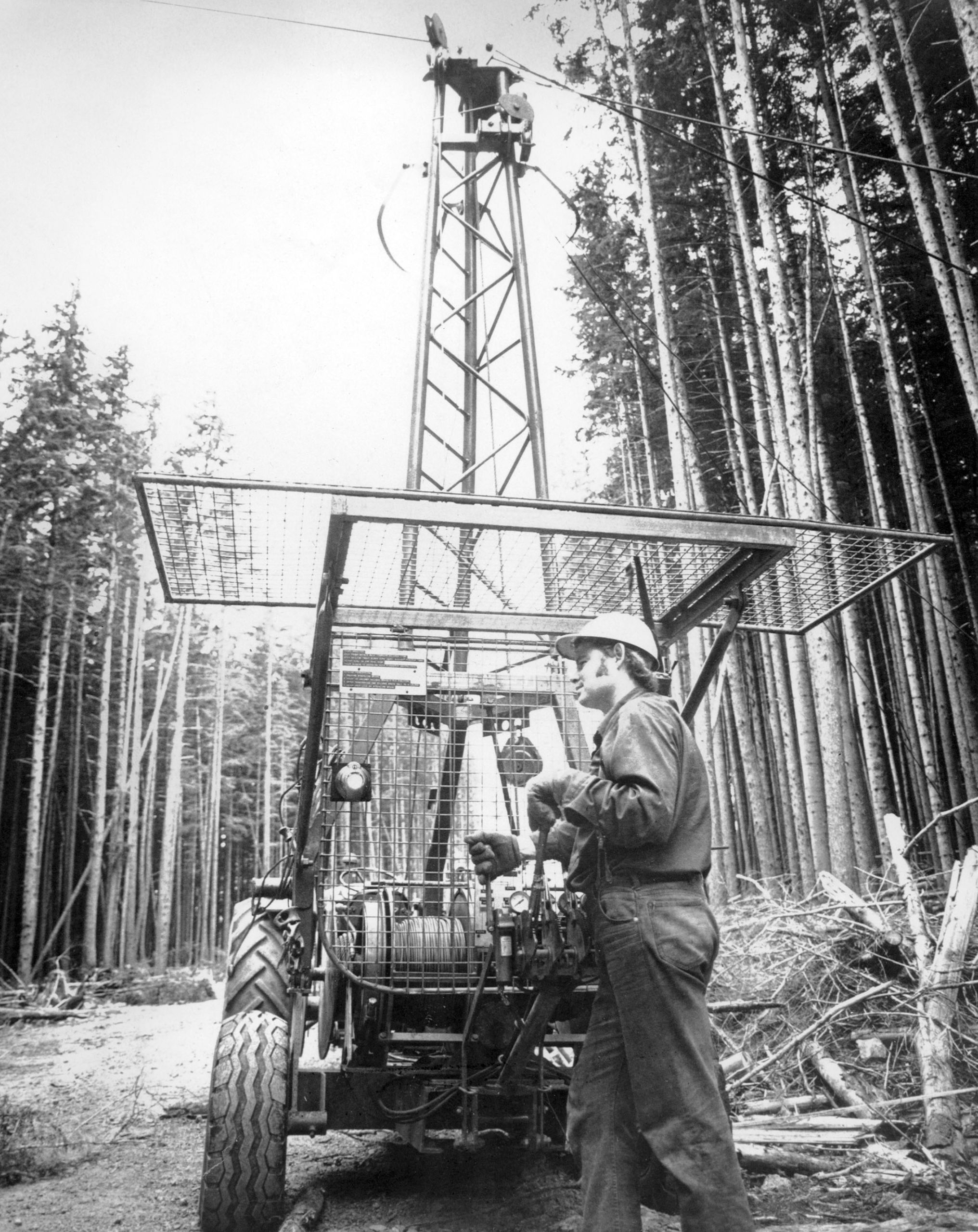 A black-and-white image of a man standing behind a logging loader