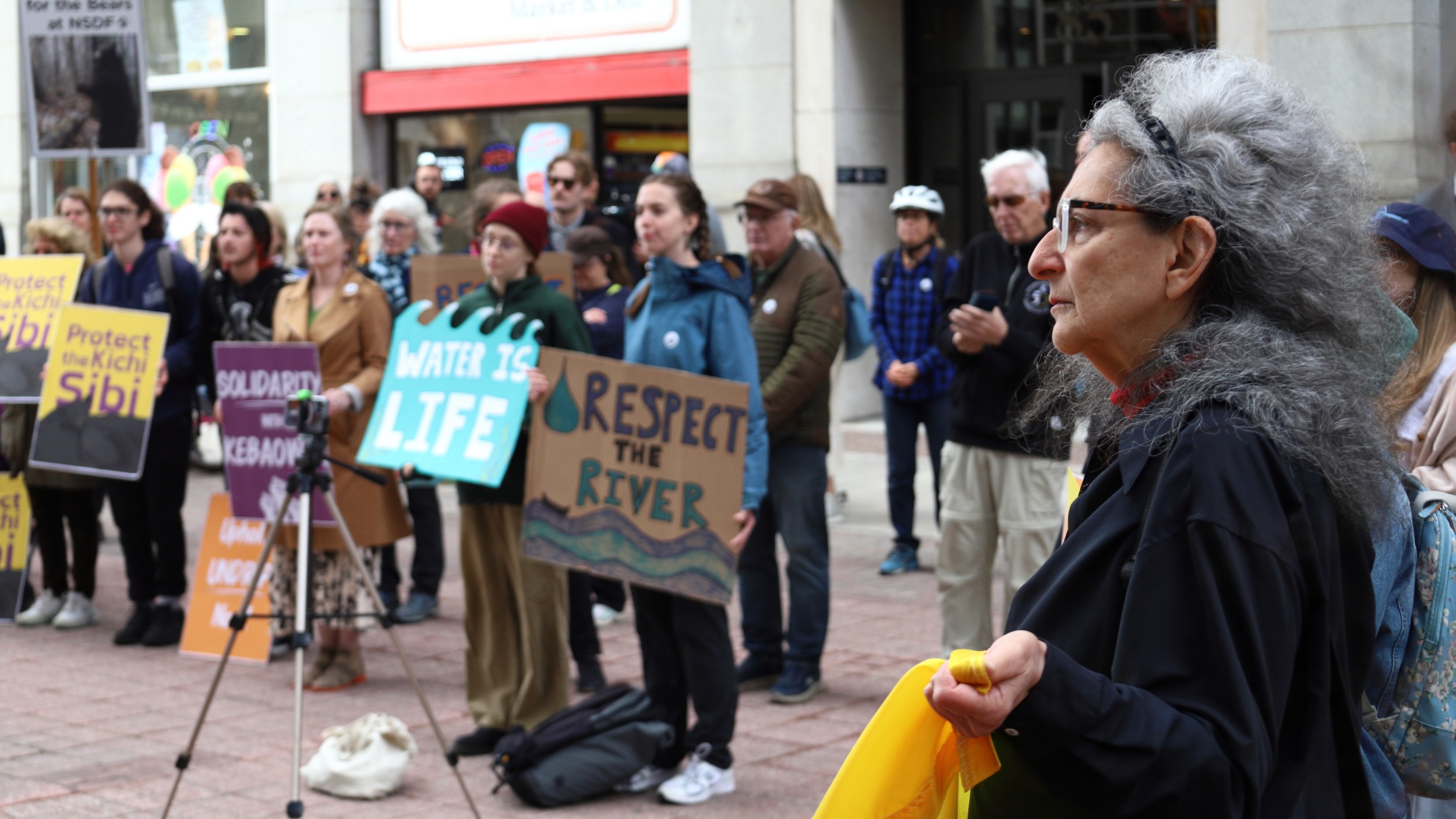 Participants in a rally hold signs with slogans such as "Water is Life" and "Respect the River."