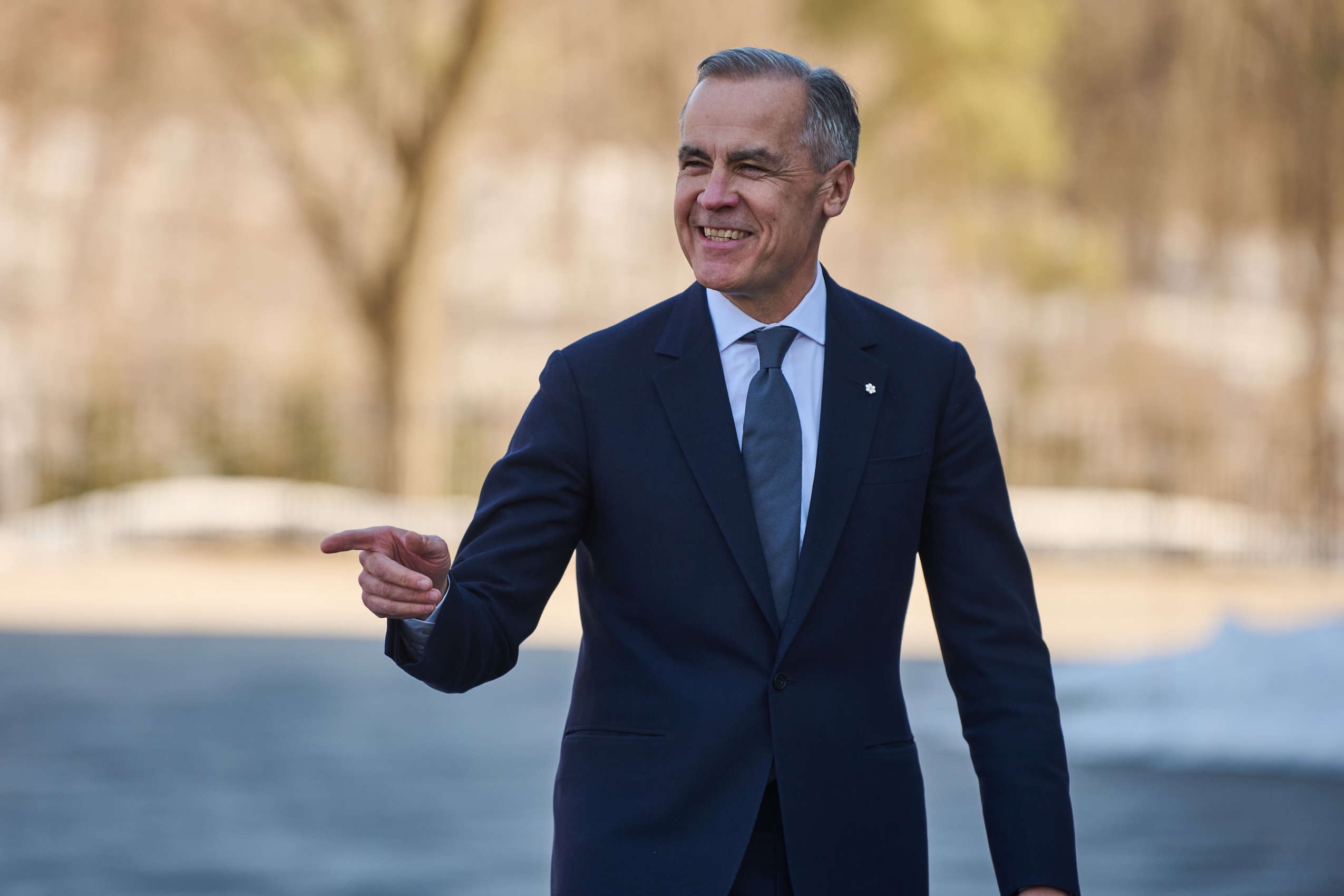 Wearing a dark suit, Prime Minister Mark Carney smiles and points as he arrives at Rideau Hall ahead of his swearing-in ceremony.