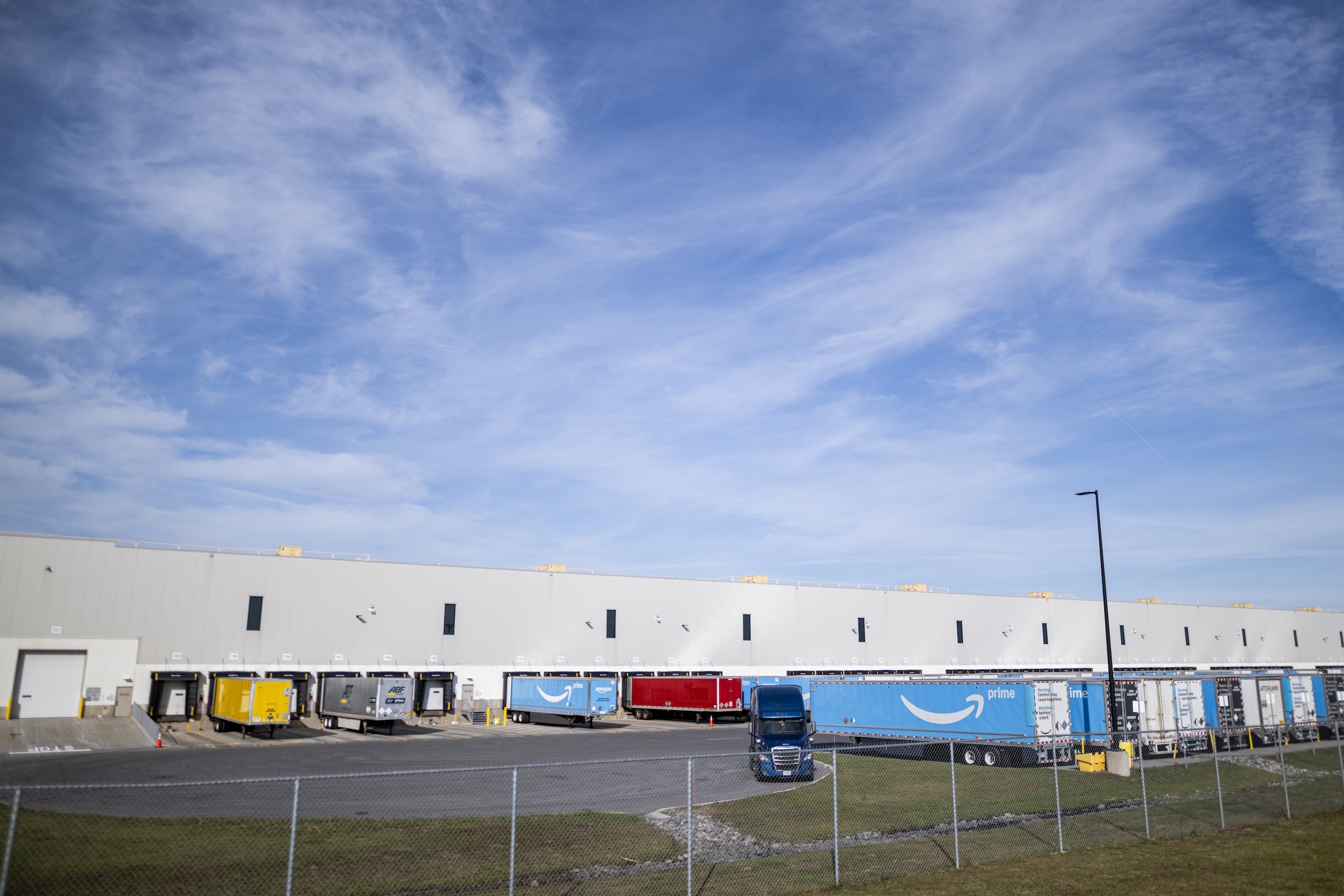Brightly coloured Amazon trucks in a parking lot outside a warehouse, under a cloudy sky.