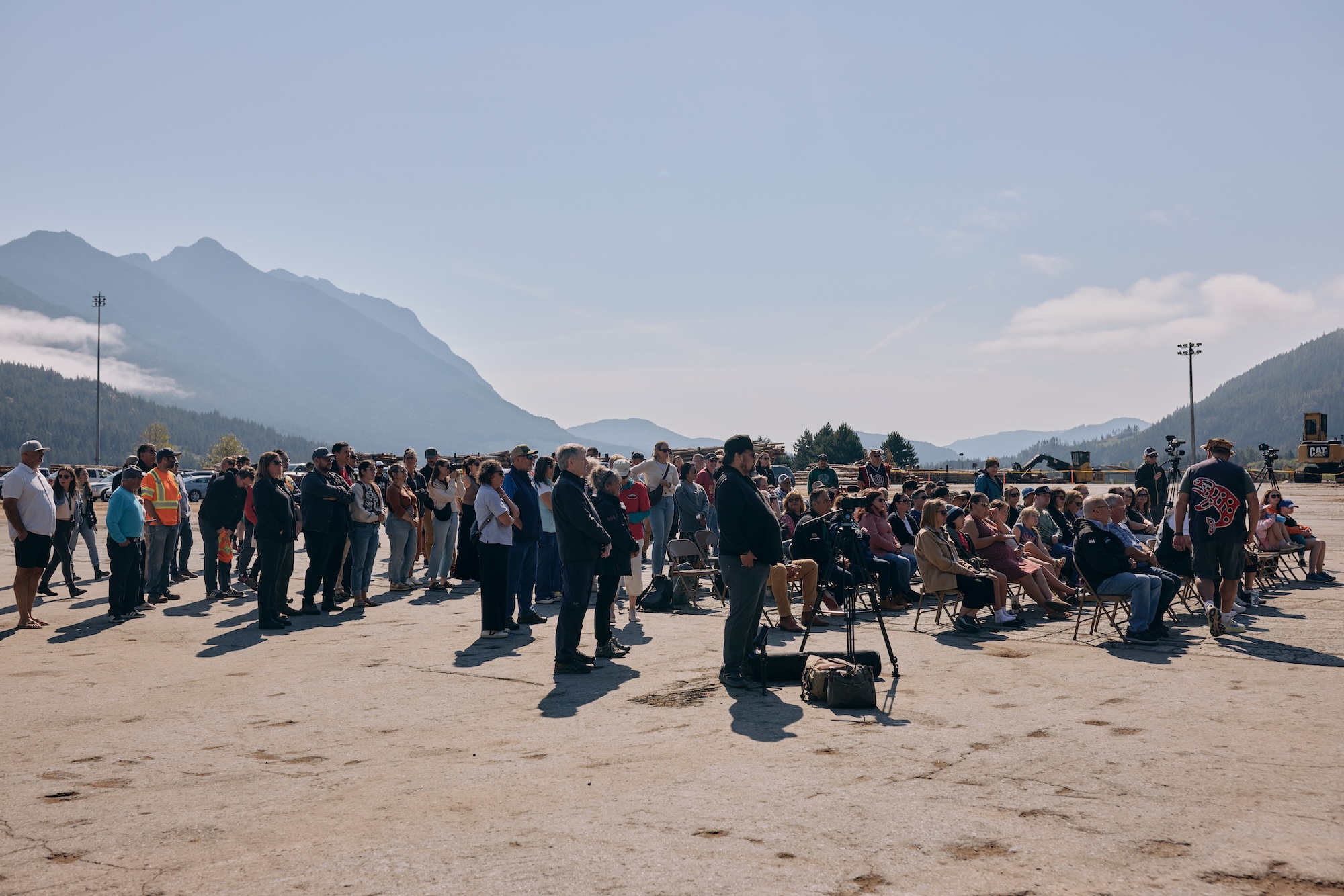 A crowd of people gathered, some sitting on chairs, under a clear sky