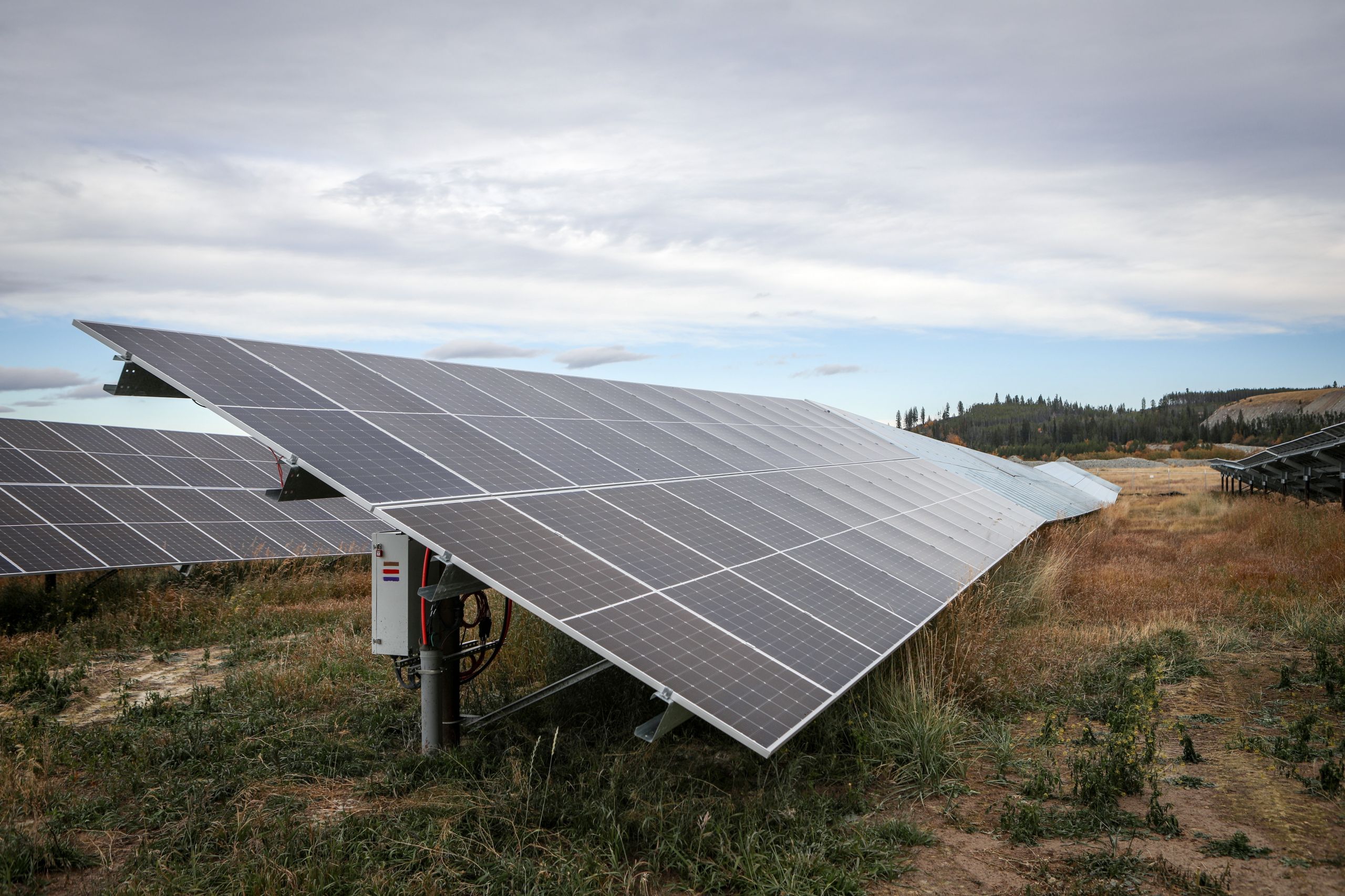 A large solar panel on a solar grid in a dry field, with low hillside in the background.