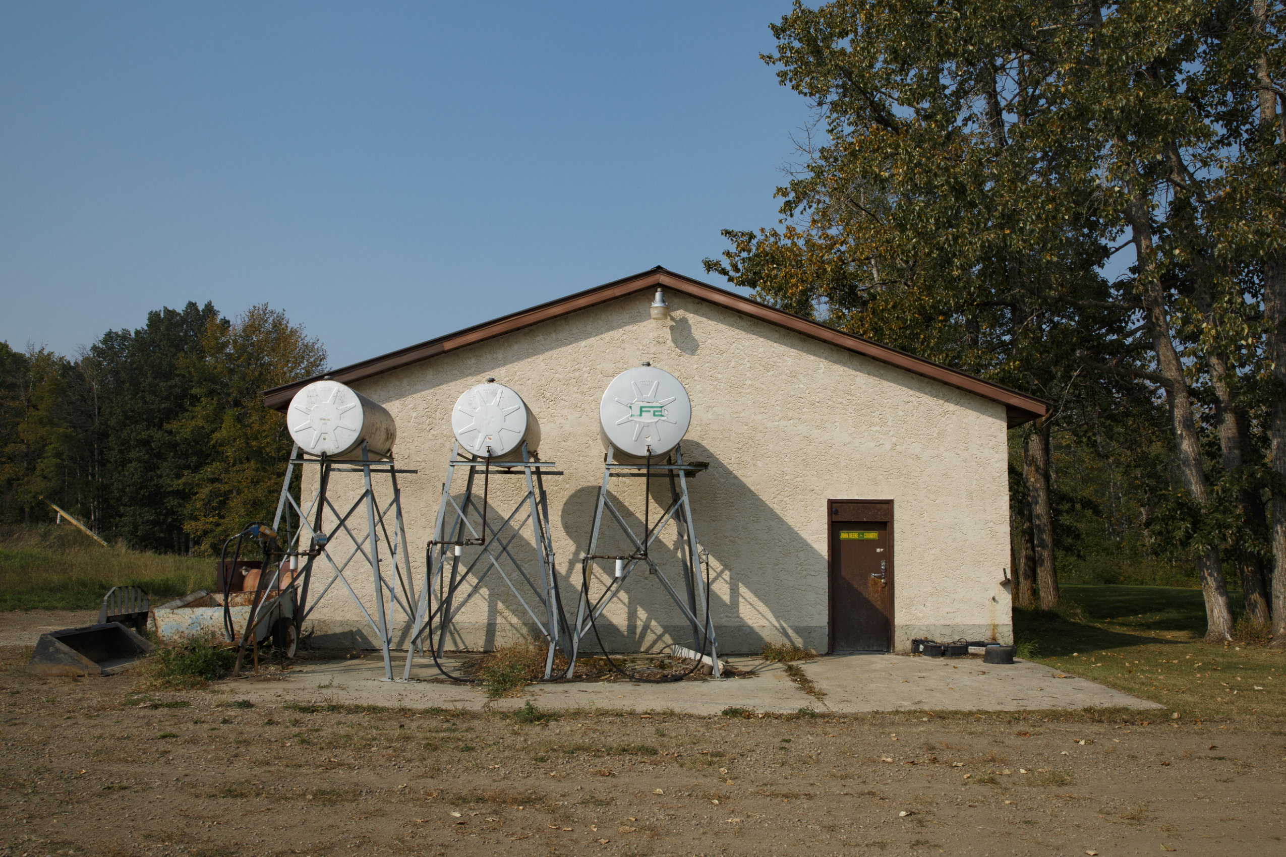 Three oil barrels atop stands against a beige-coloured farm building.