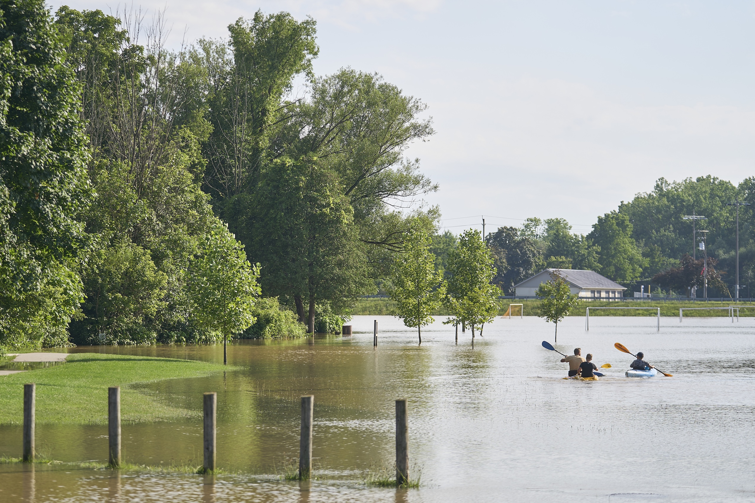 Three people in kayaks paddle away from the camera on a flooded soccer field in Strathroy, Ontario.