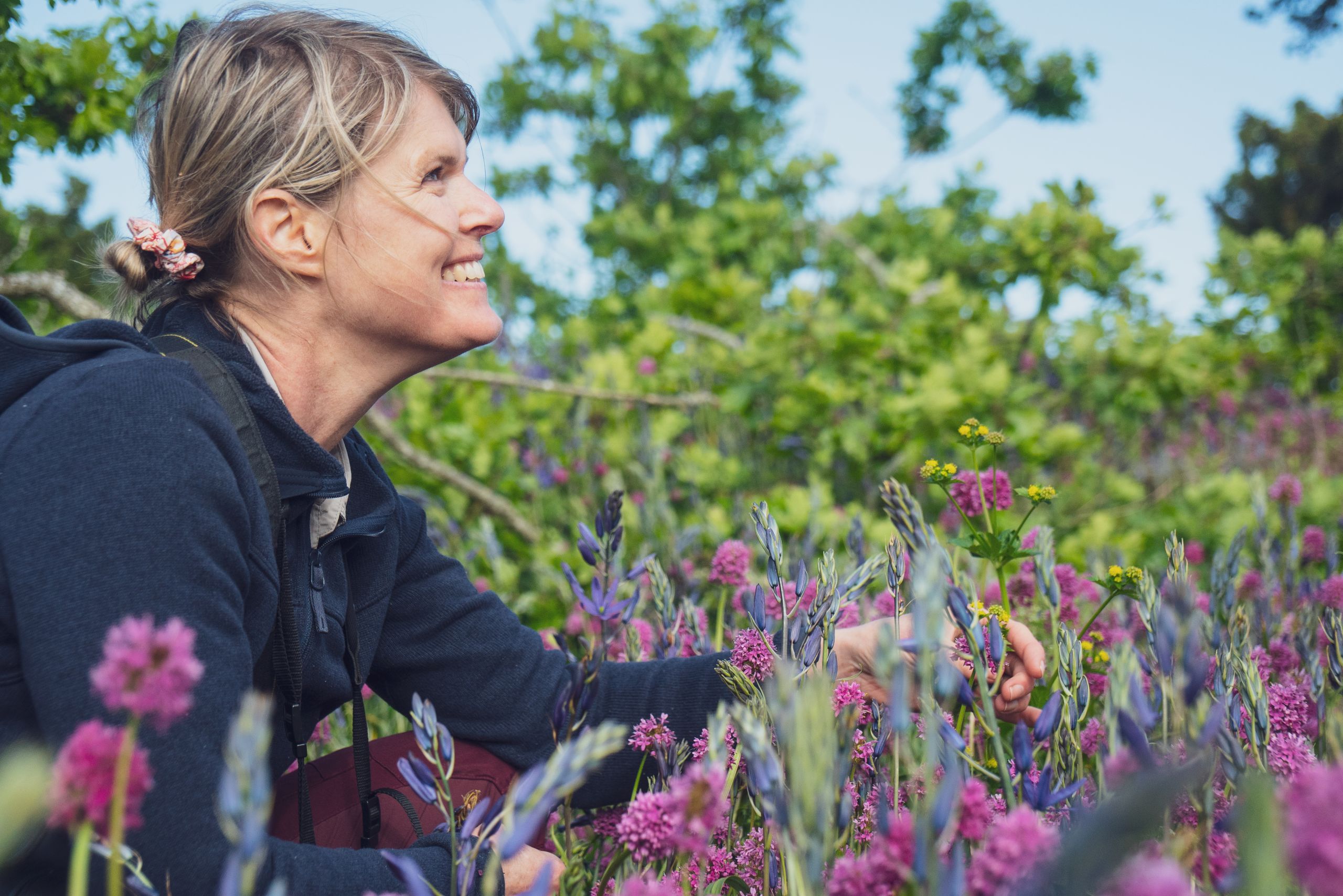 Tara Martin kneels, smiling, in a meadow of abundant wildflowers