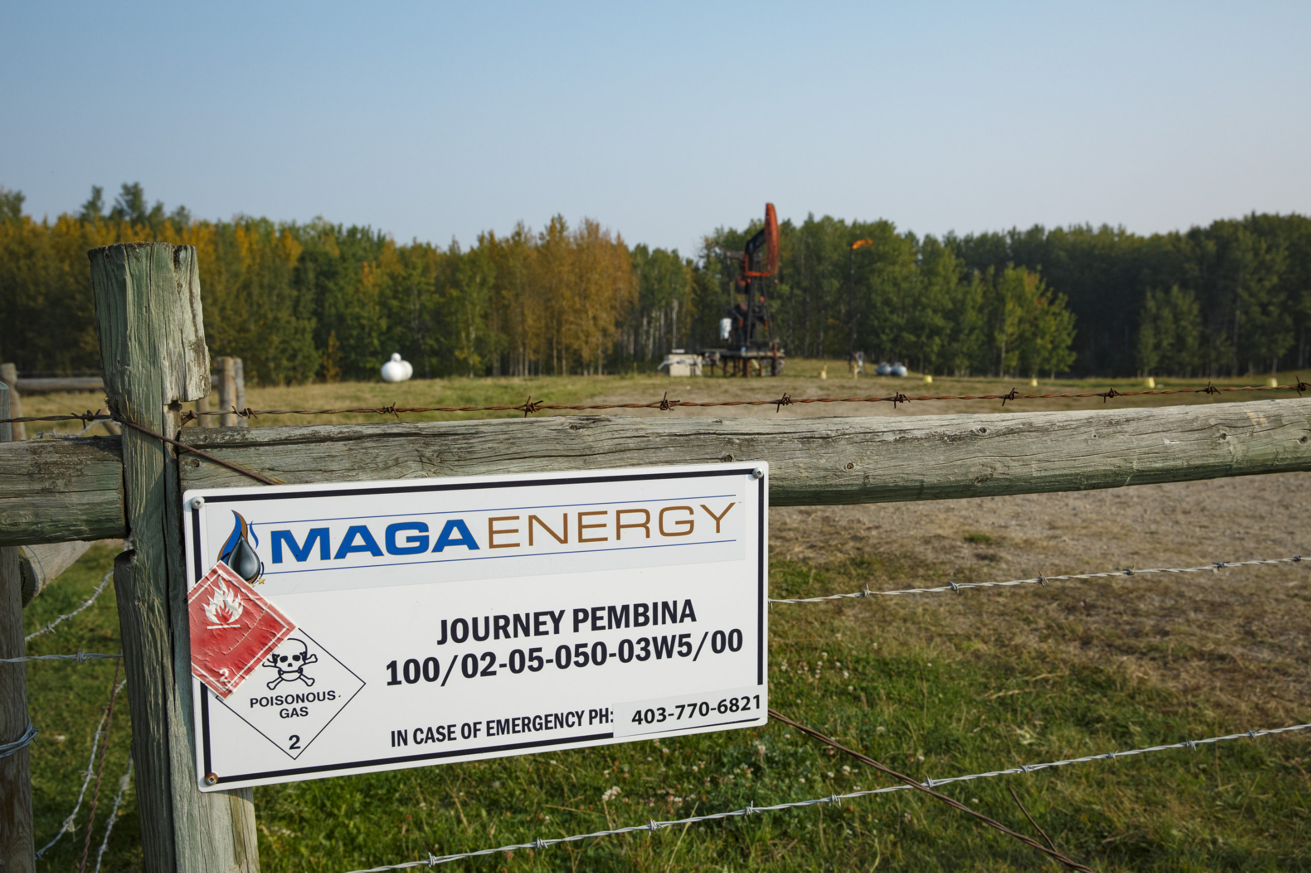 In the foreground, a sign on a fence post reads "MAGA ENERGY." There is a pump jack operating in a field in the background.