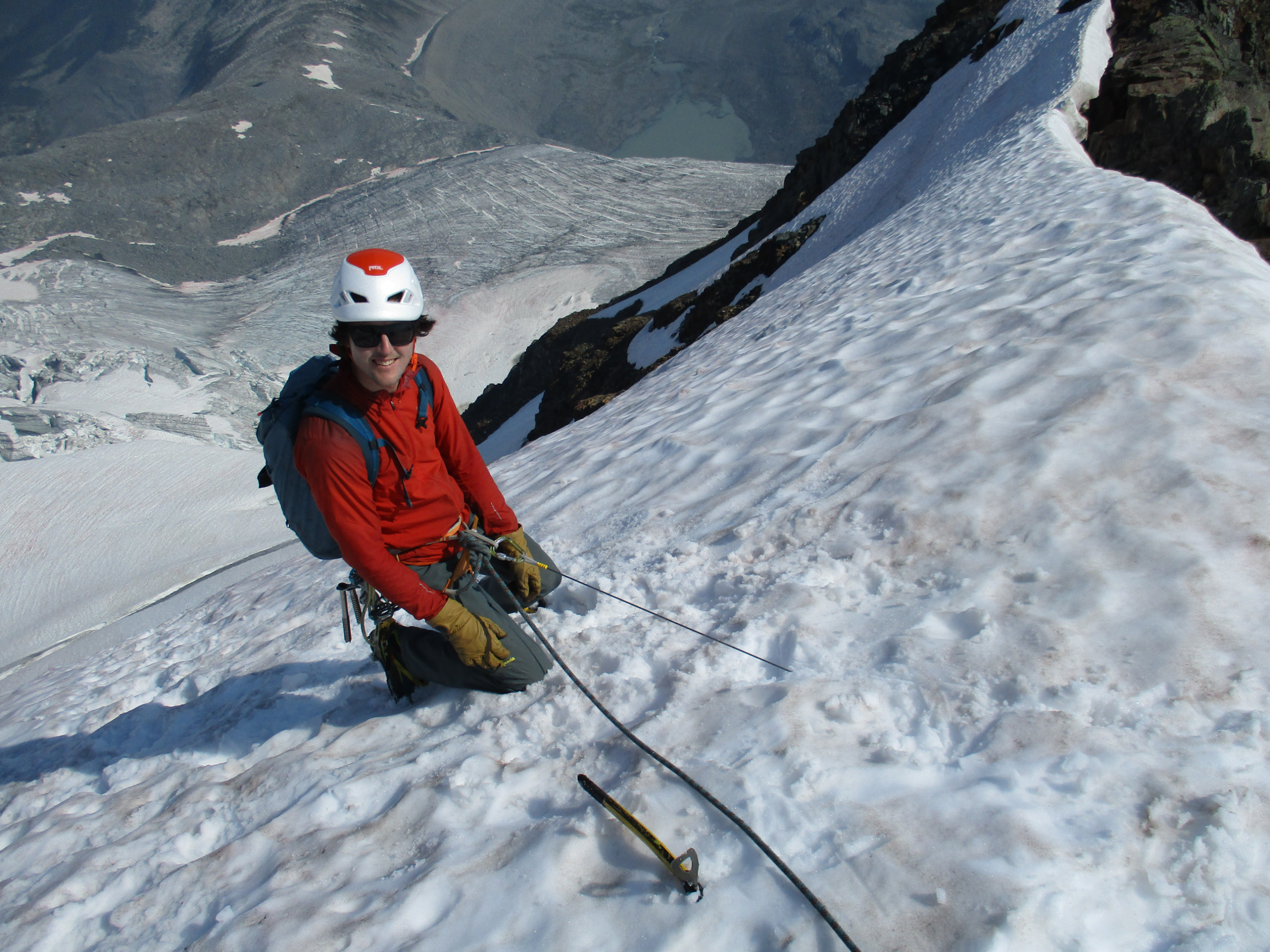 An alpine climber rests on his knees on a steep snowy slope.
