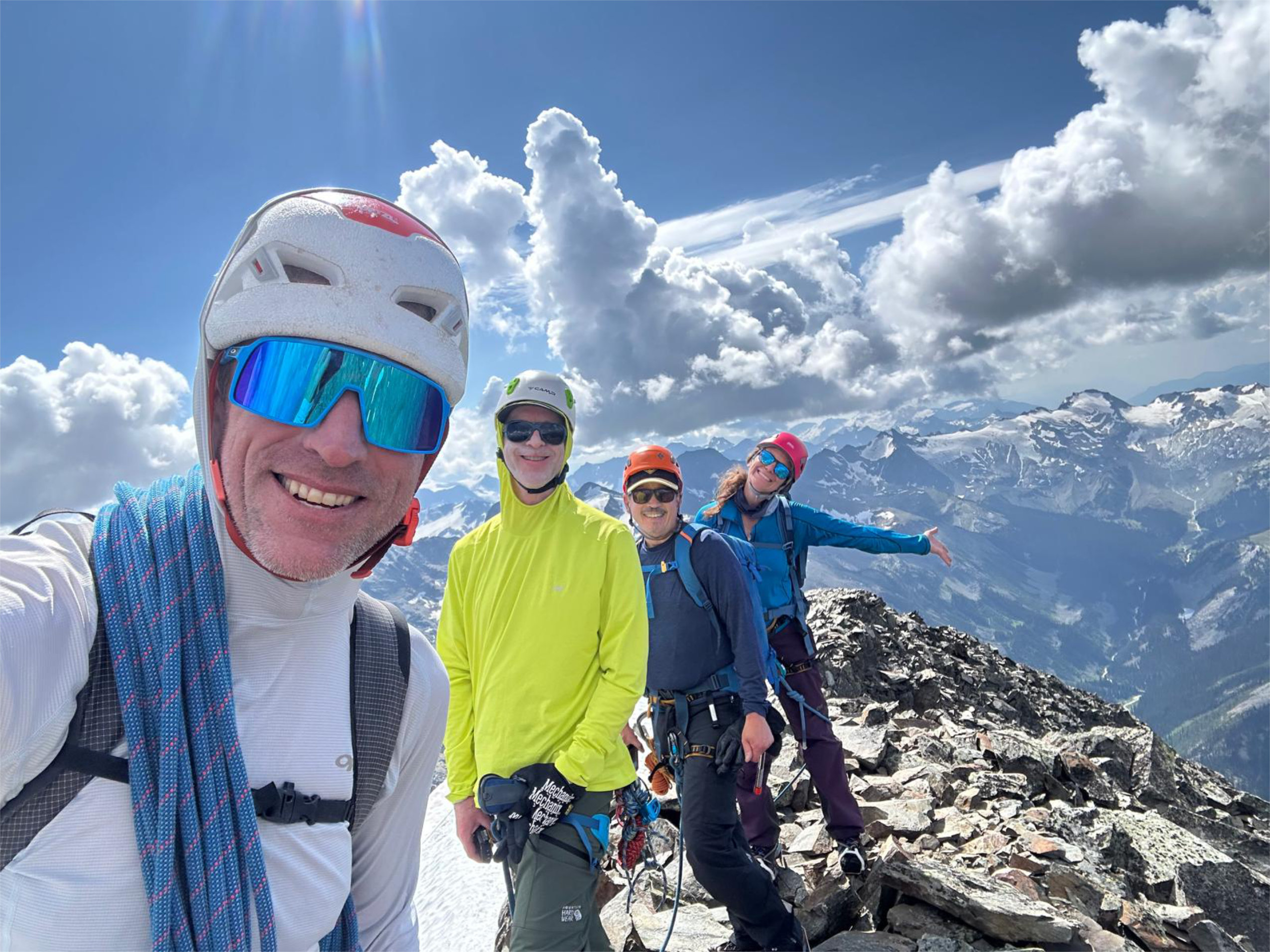 Four alpine climbers pose for a selfie on what appears to be a summit.