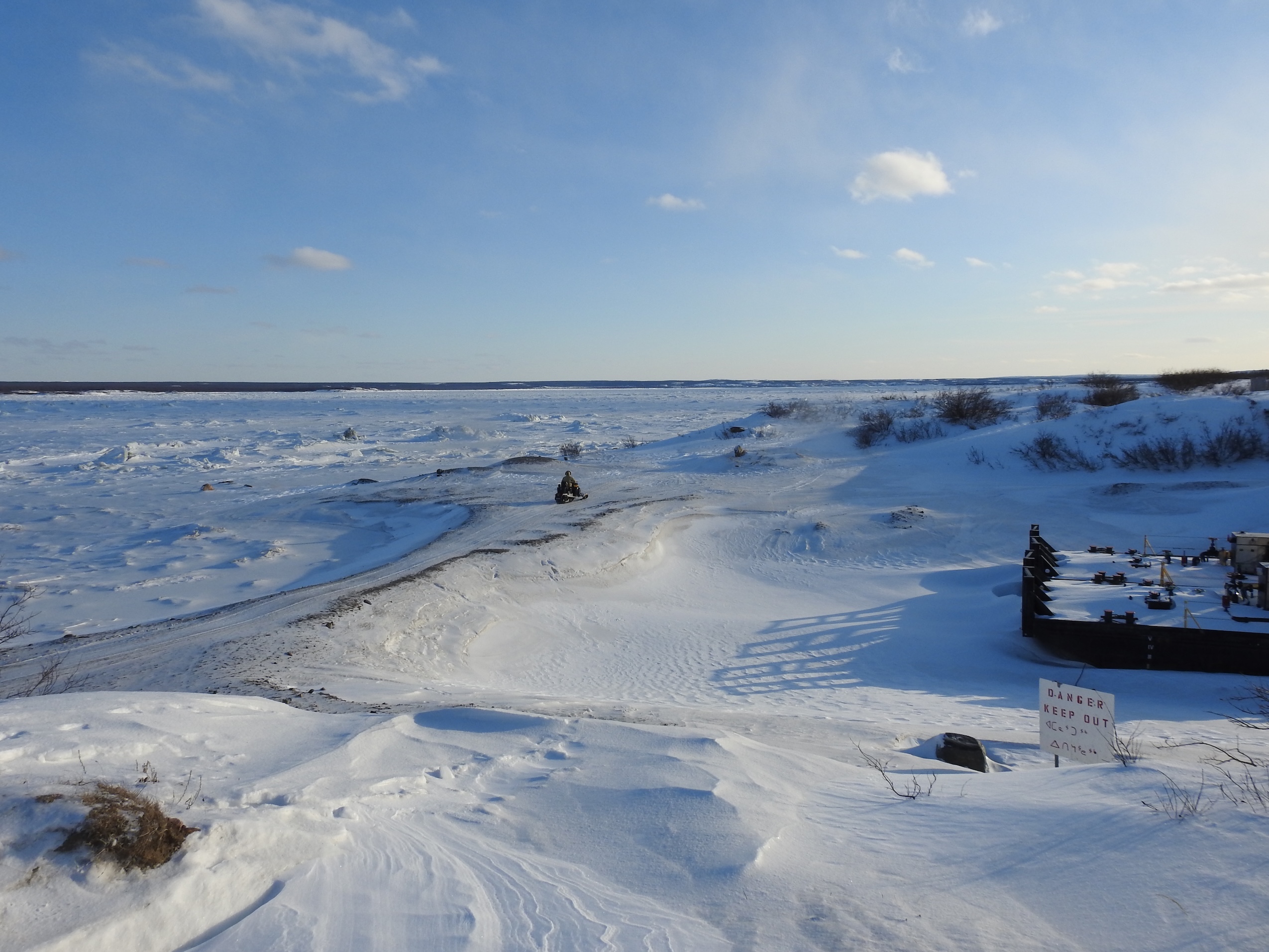 A frozen-over port on an icy landscape, with the tail end of an old boat sticking out of the ice on the right.