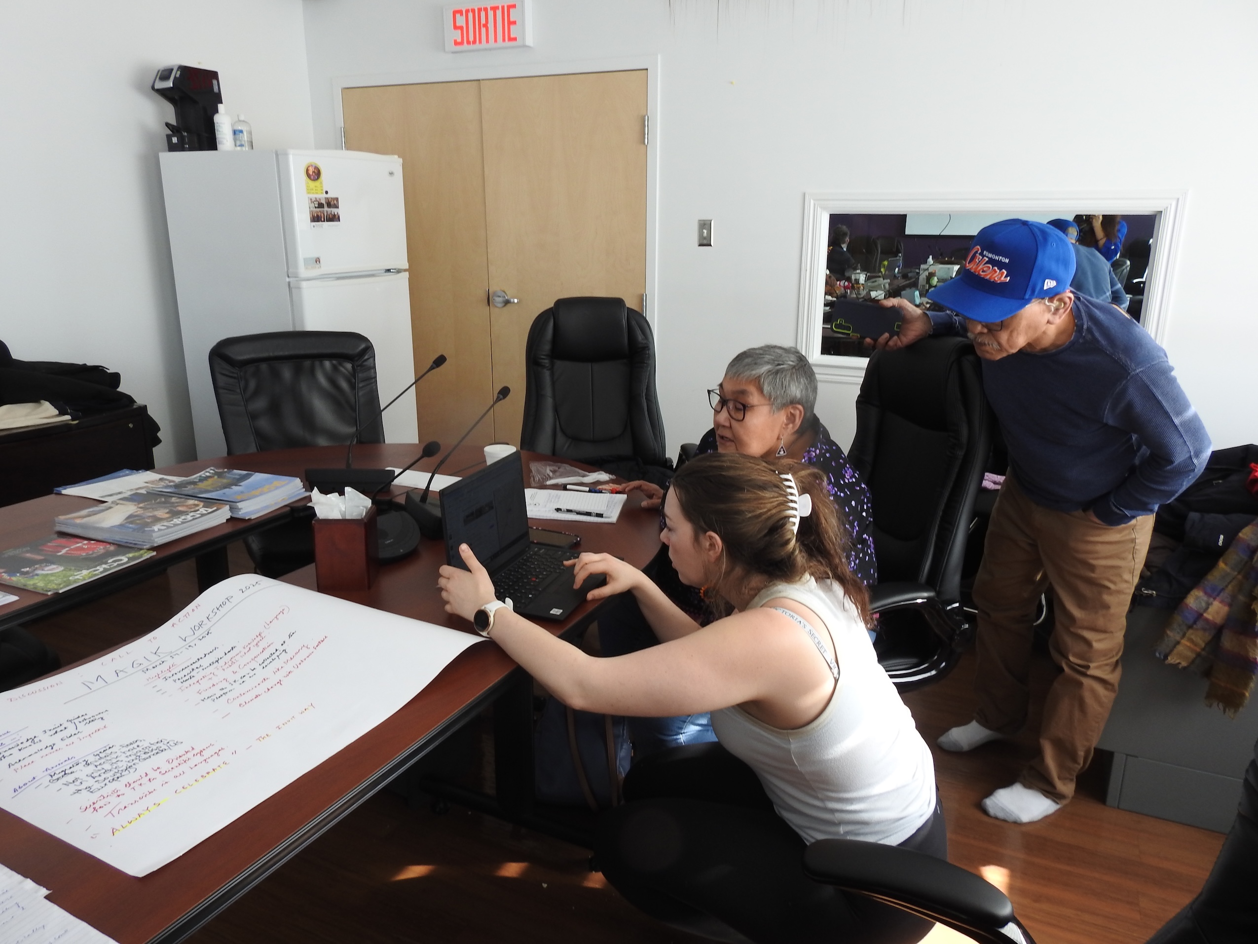 Three people, including one Inuit Elder, review a computer screen together.