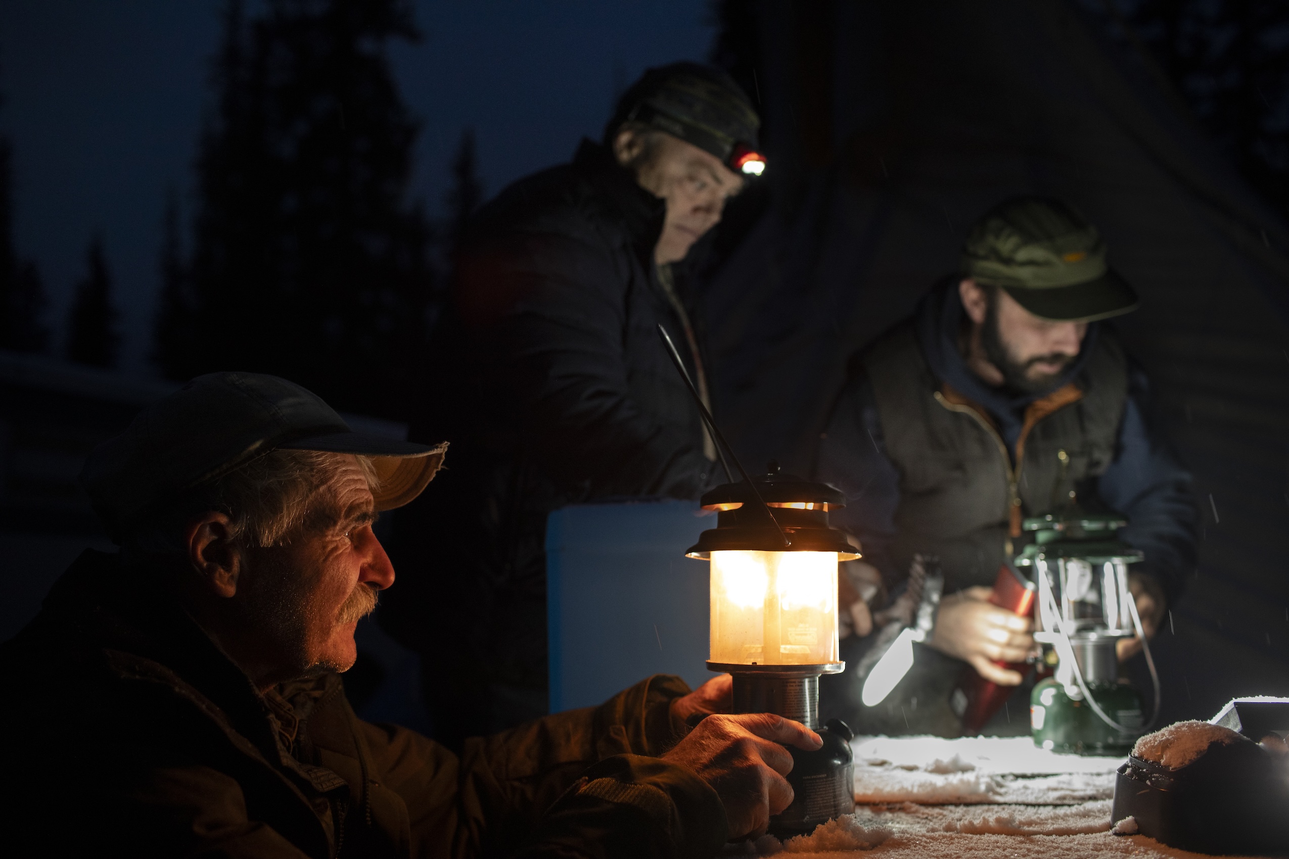 Three men gather around a lamp in the dark.