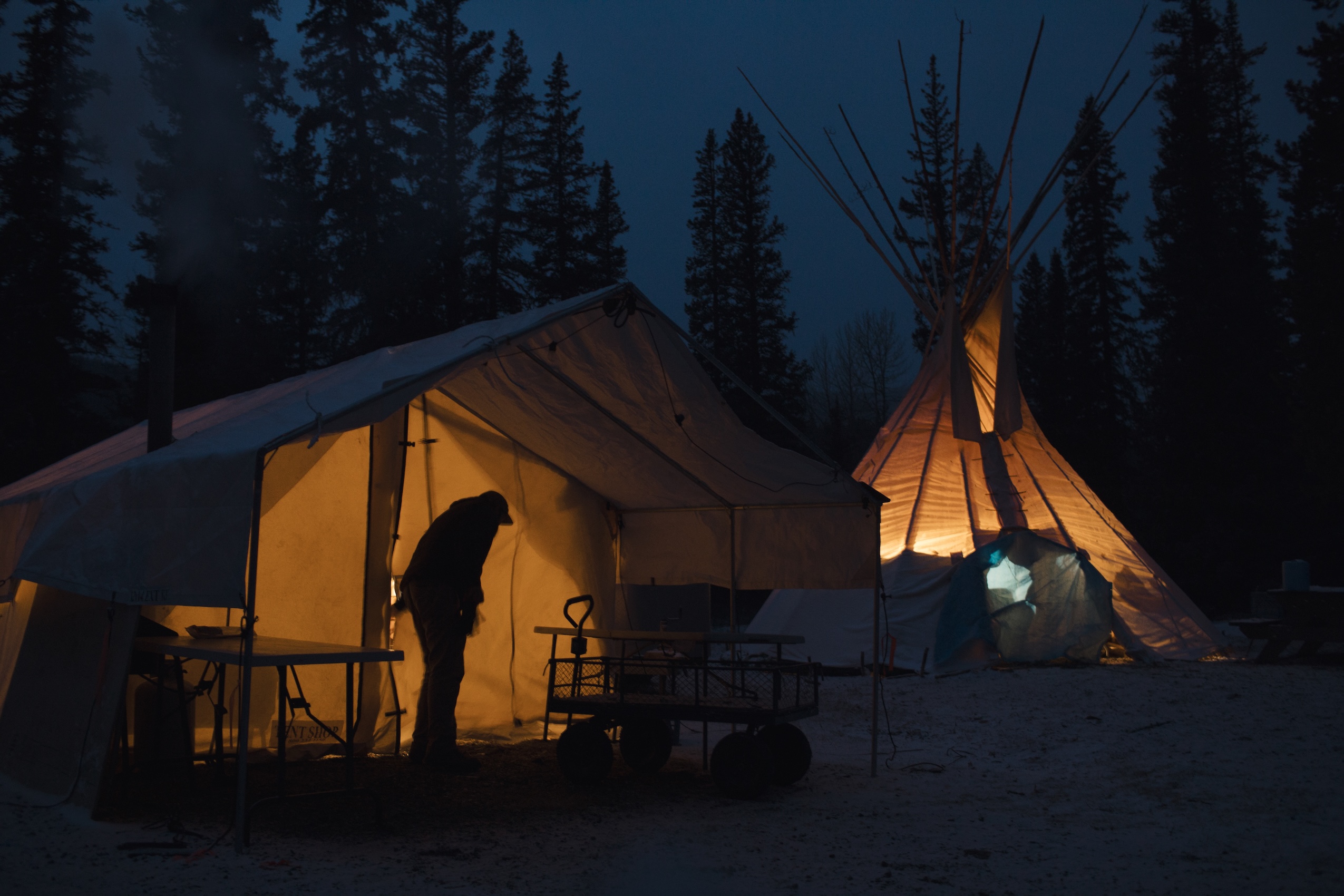A man's silhouette against a camp tent, illuminated by light from inside.