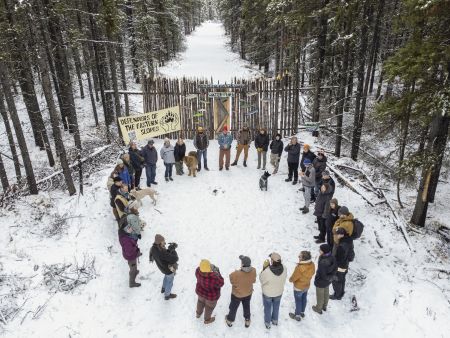 A group of people gathers in a circle on snowy ground at the edge of a forest.