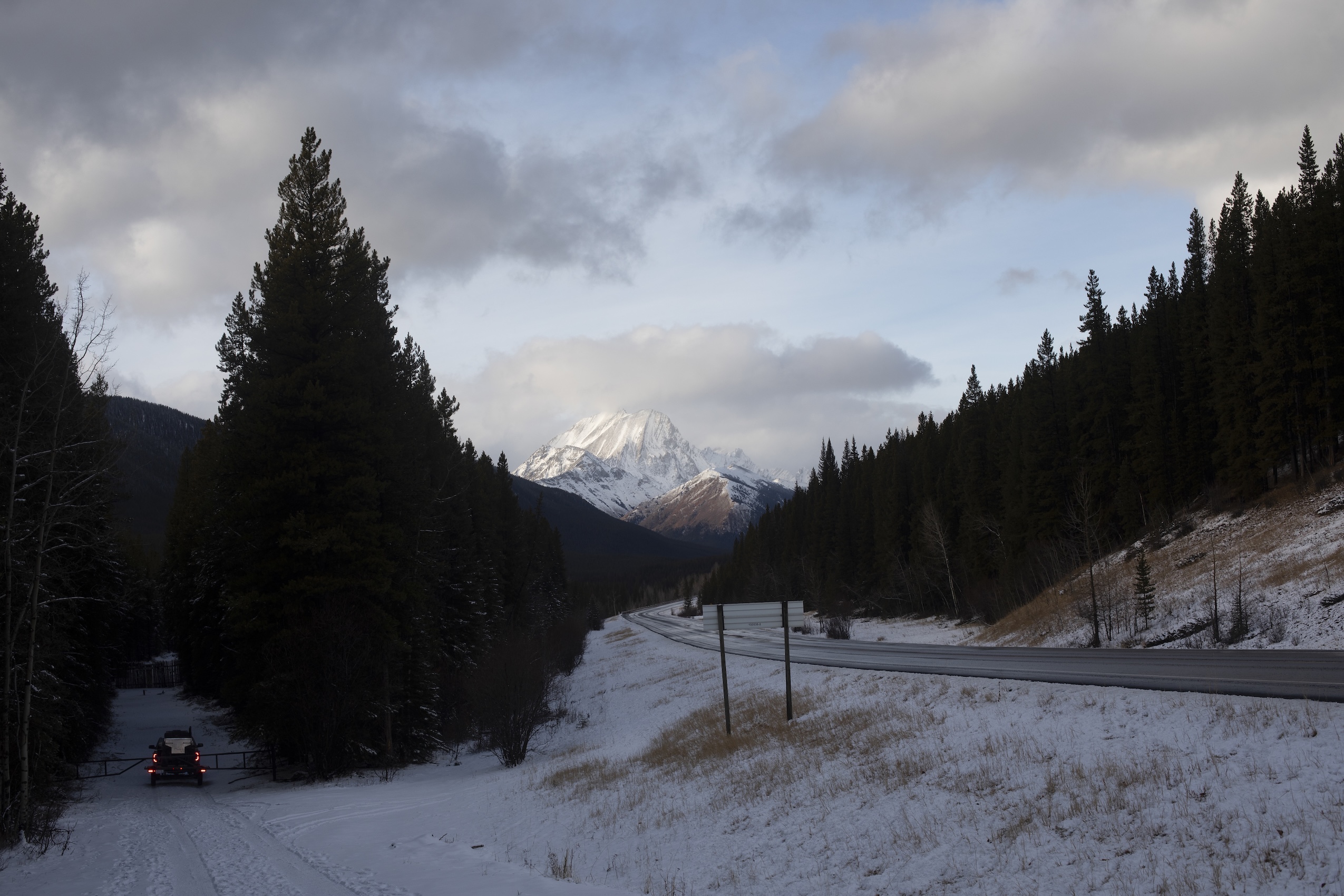 A truck drives down a snowy road off a highway.
