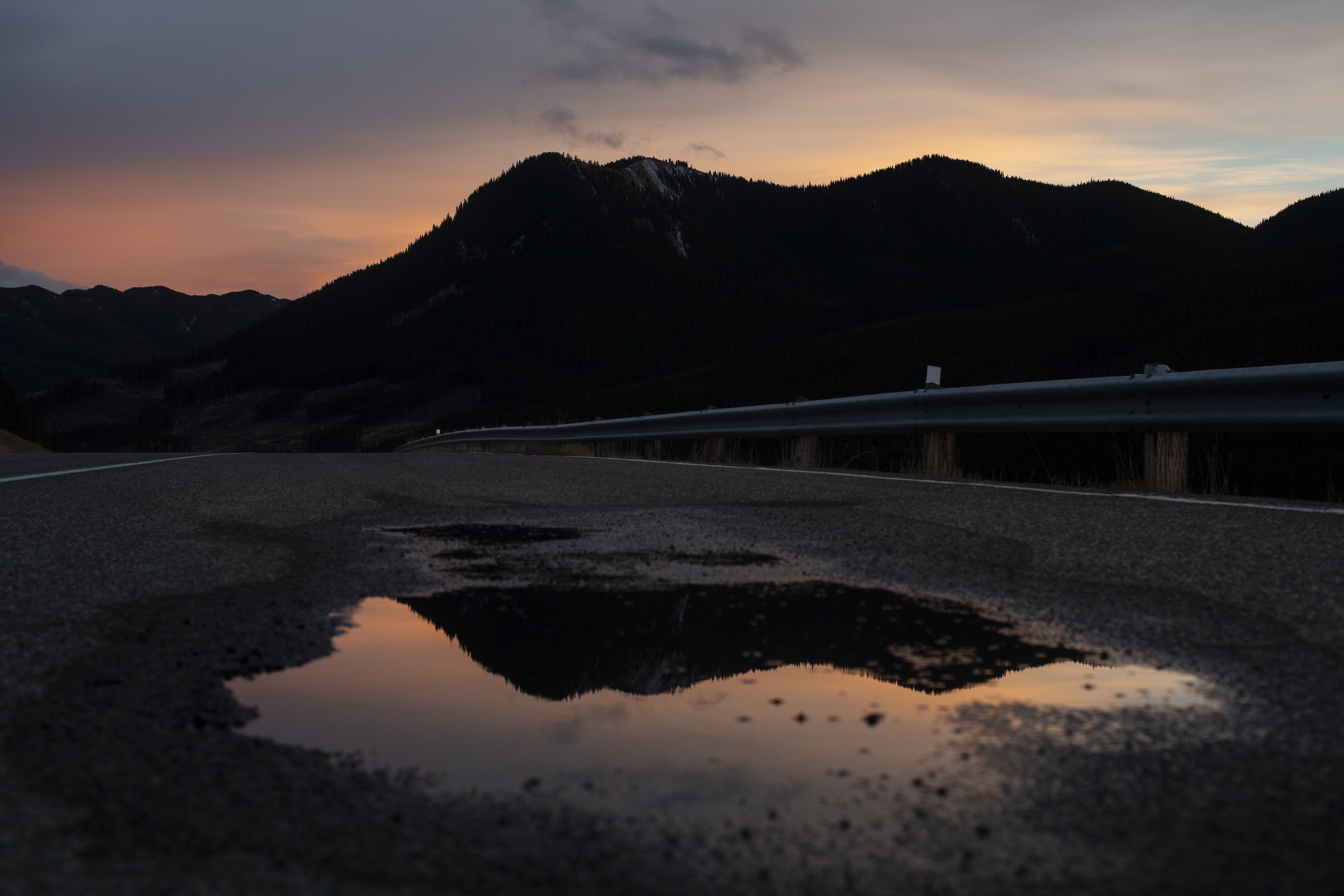 A mountainside reflected in a pool of a water on a highway at dusk.