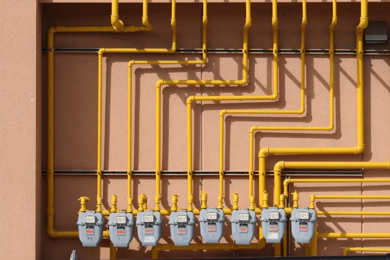 A bay of Enbridge Gas meters connected to a series of yellow pipes in front of a brown wall.