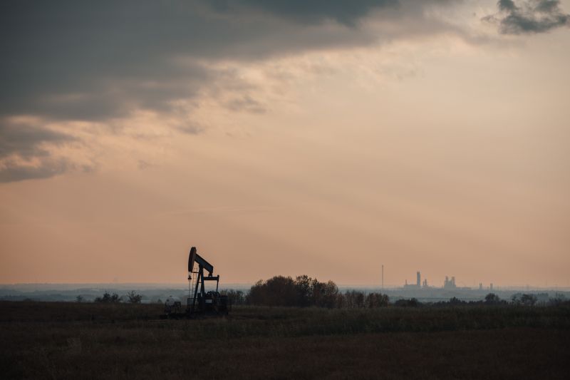 Orange sky with single pumpjack in the middle distance and more industrial activity on the horizon.