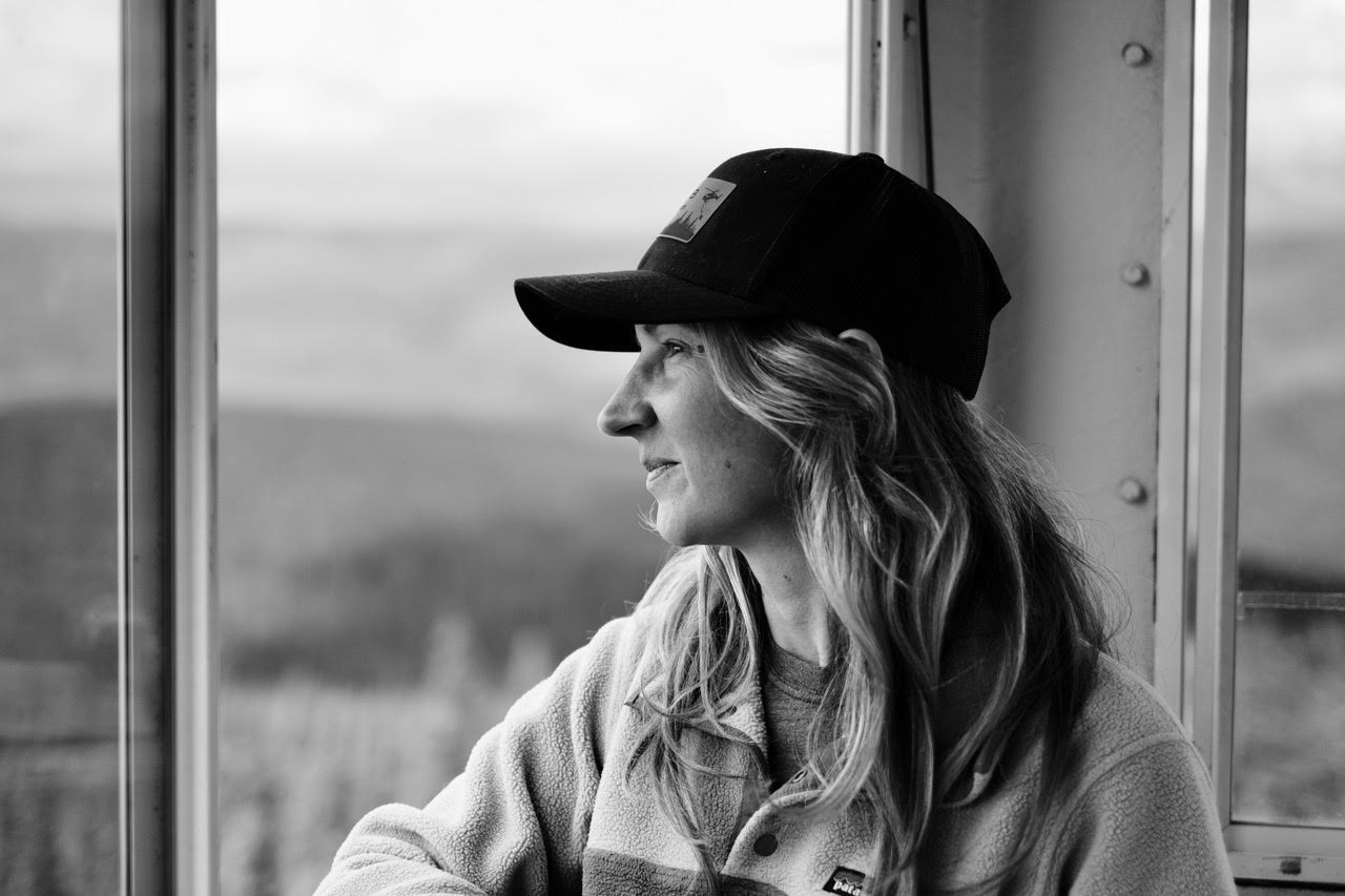 A black-and-white photo of a woman staring off to her right, wearing a ball cap.
