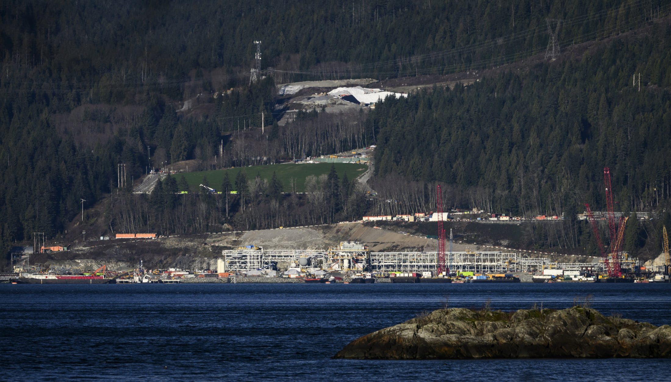 The Woodfibre LNG site, photographed from across Howe Sound in Squamish, B.C. Cranes and other industrial equipment are situated on shoreline.