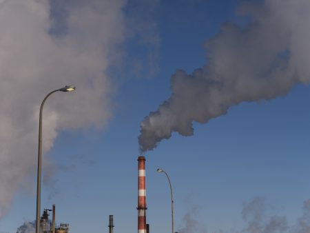 A red-and-white striped smokestack emits a grey cloud a smoke into the air wintry air.