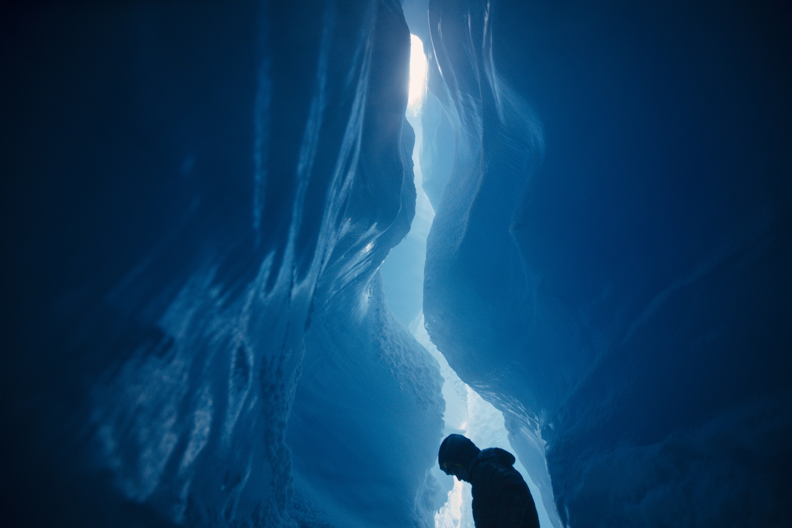 The dark shadow of a person is in the bottom of the frame surrounded by the walls of a glacier
