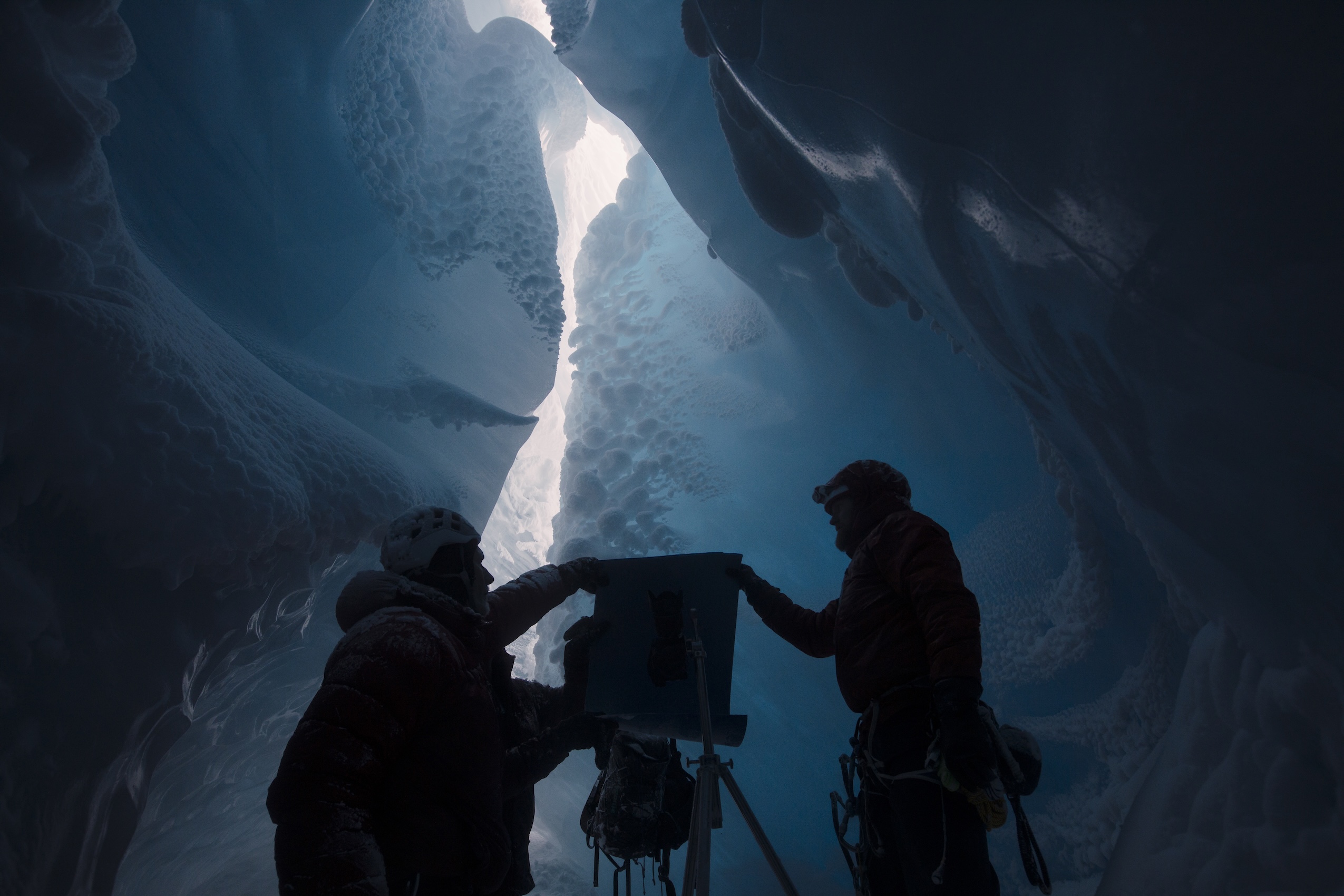 Two men hold camera equipment in shadows in glacier