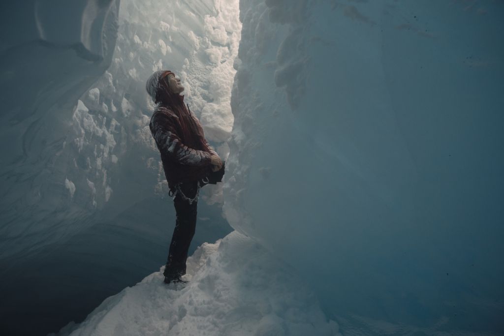 A man standing inside of a glacier looks up at the sunshine