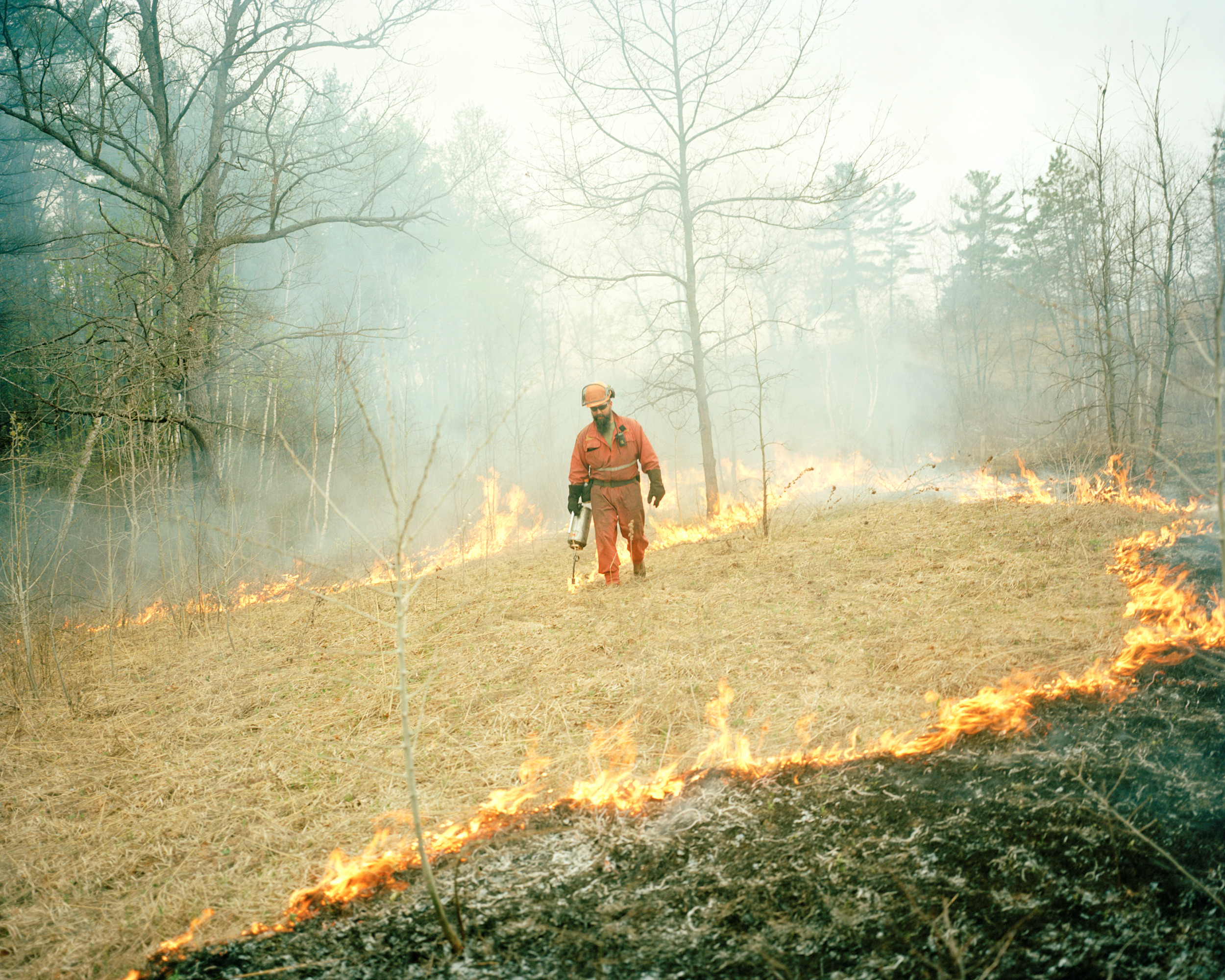 A man in orange coveralls and a helmet sets a controlled burn in the Alderville Black Oak Savanna
