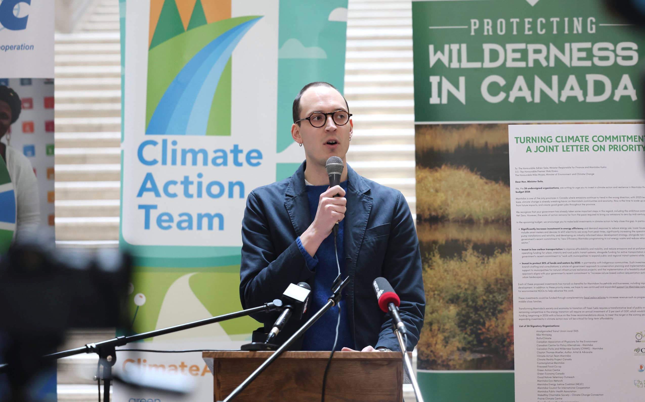 Niall Harney speaks into microphones at a press conference about climate action in Winnipeg, Manitoba.